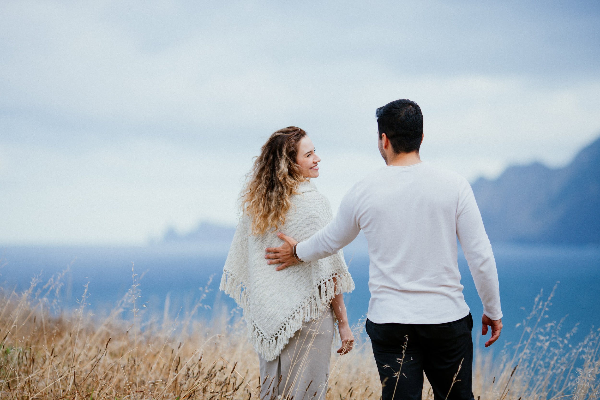 Isabela smiling back at Lucas as they walk through the grass, his hand on her back, Miradouro do Guindaste, Madeira