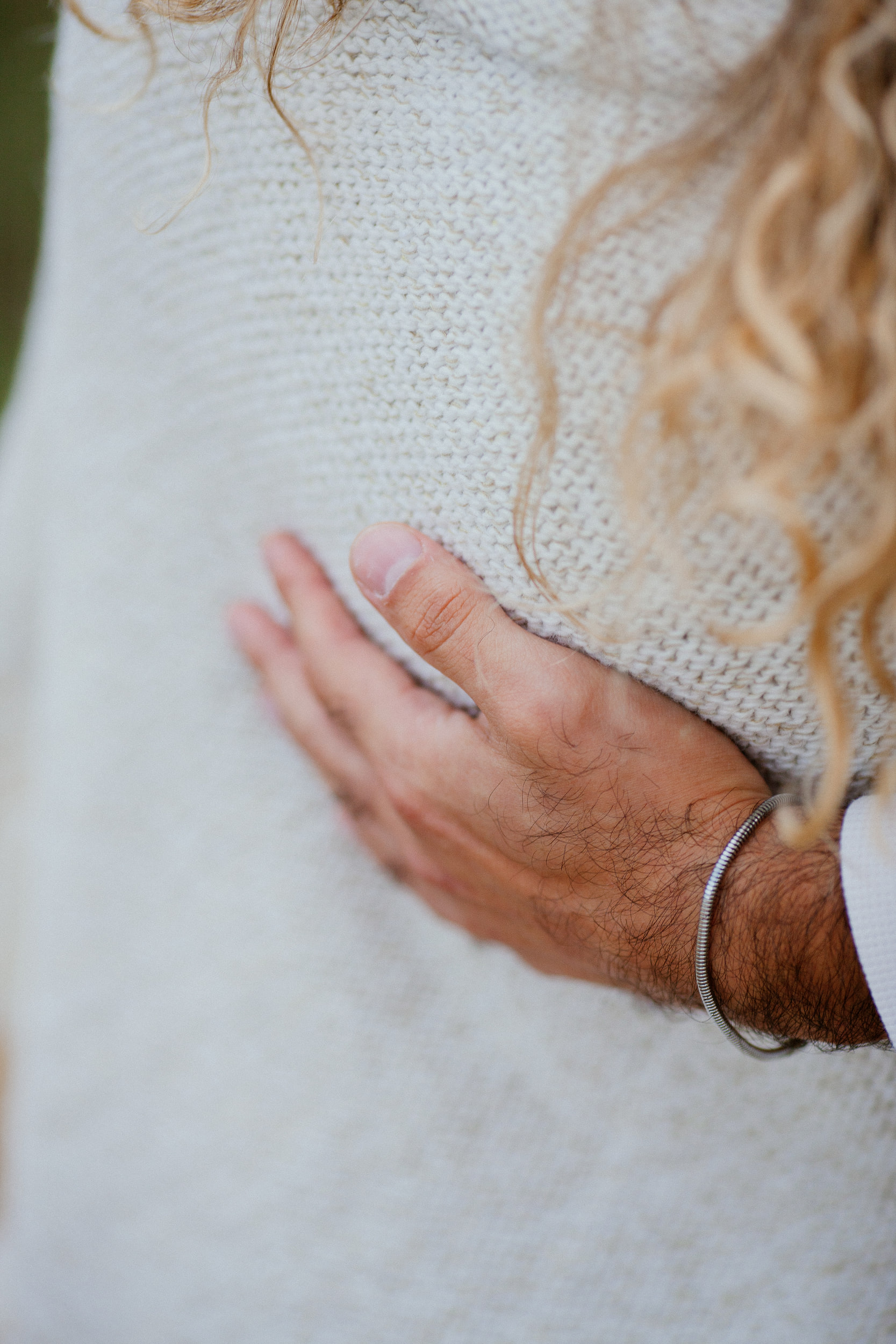 Detail of Lucas's hand with a silver bangle resting on Isabela's knit wrap, Miradouro do Guindaste, Madeira