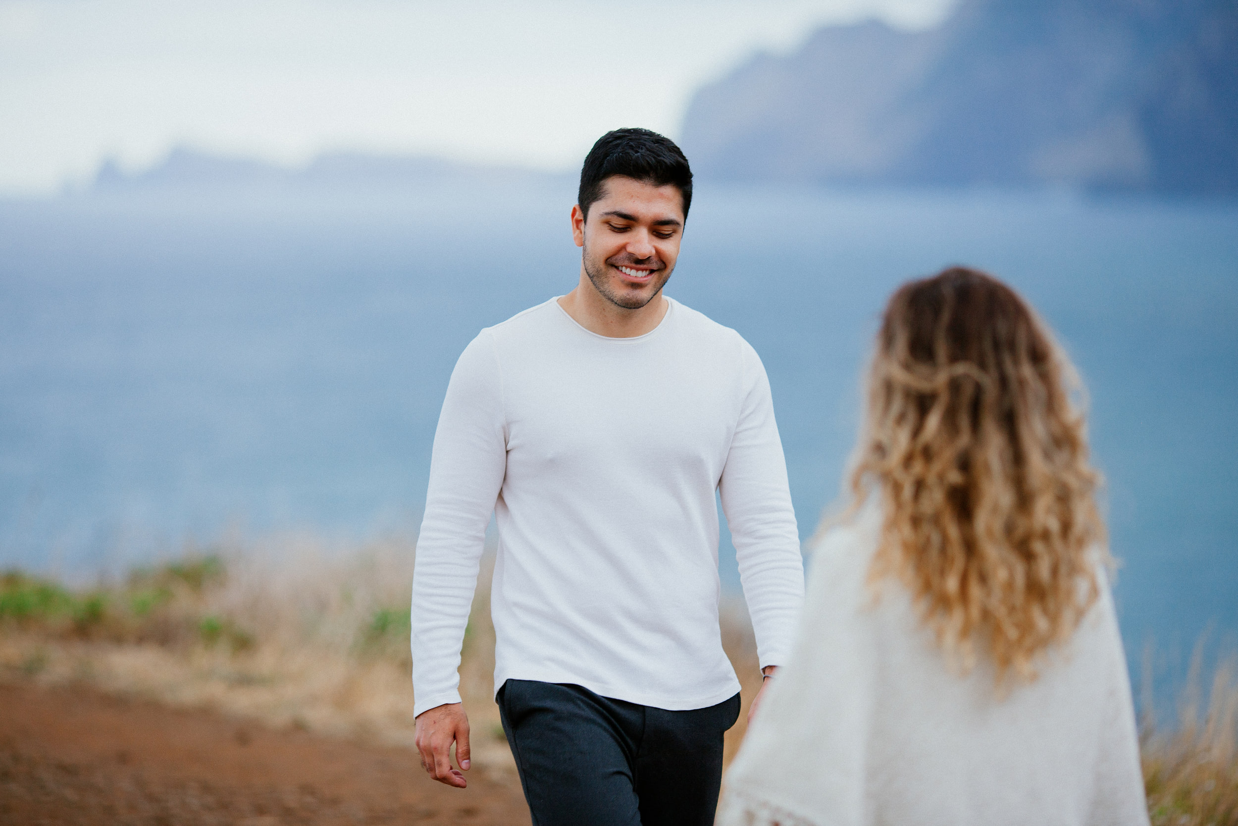 Lucas smiling down as he walks up to Isabela, sea cliffs in the haze behind, Miradouro do Guindaste, Madeira