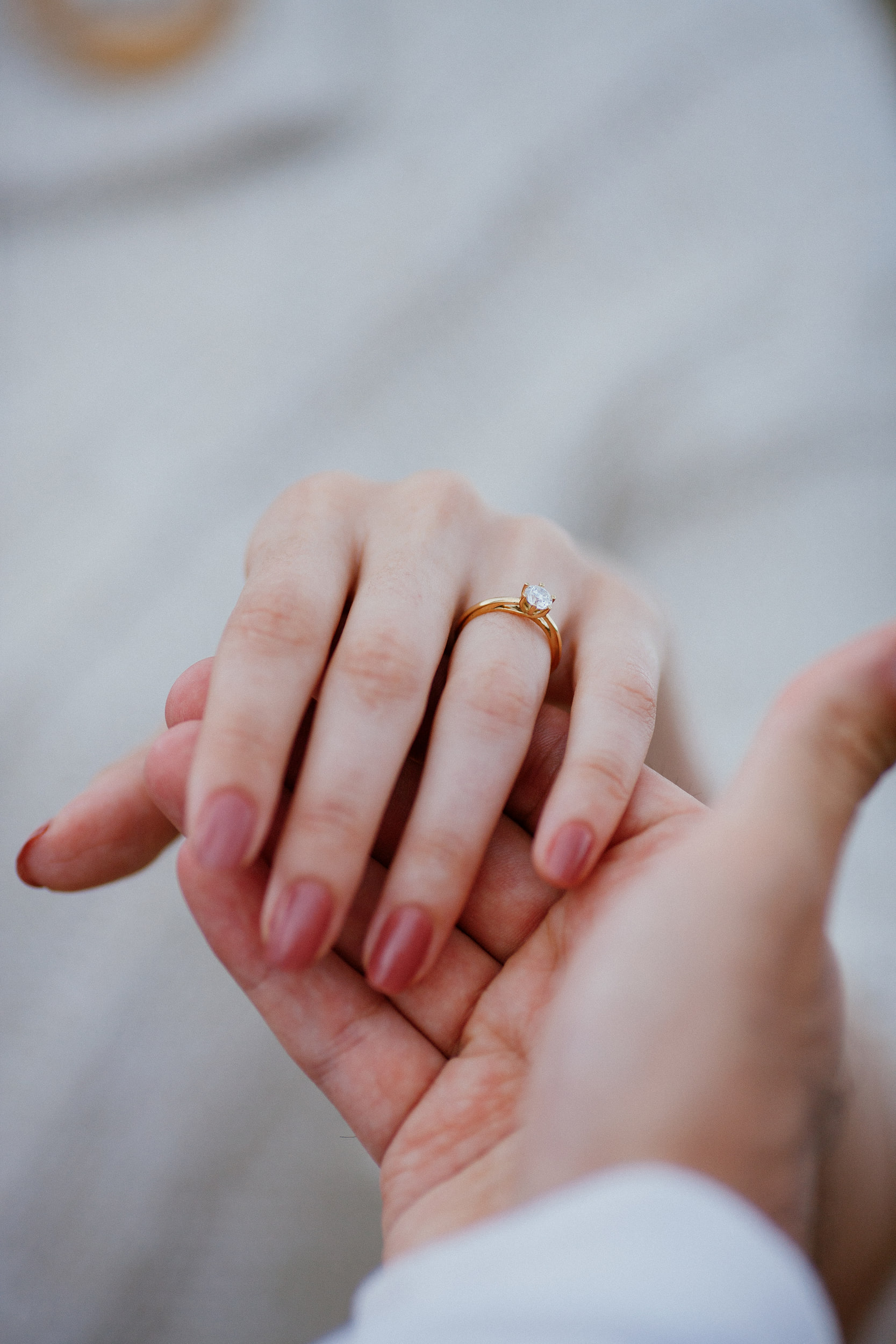 Isabela's ring hand resting in Lucas's palm, her knit wrap blurred behind, Miradouro do Guindaste, Madeira