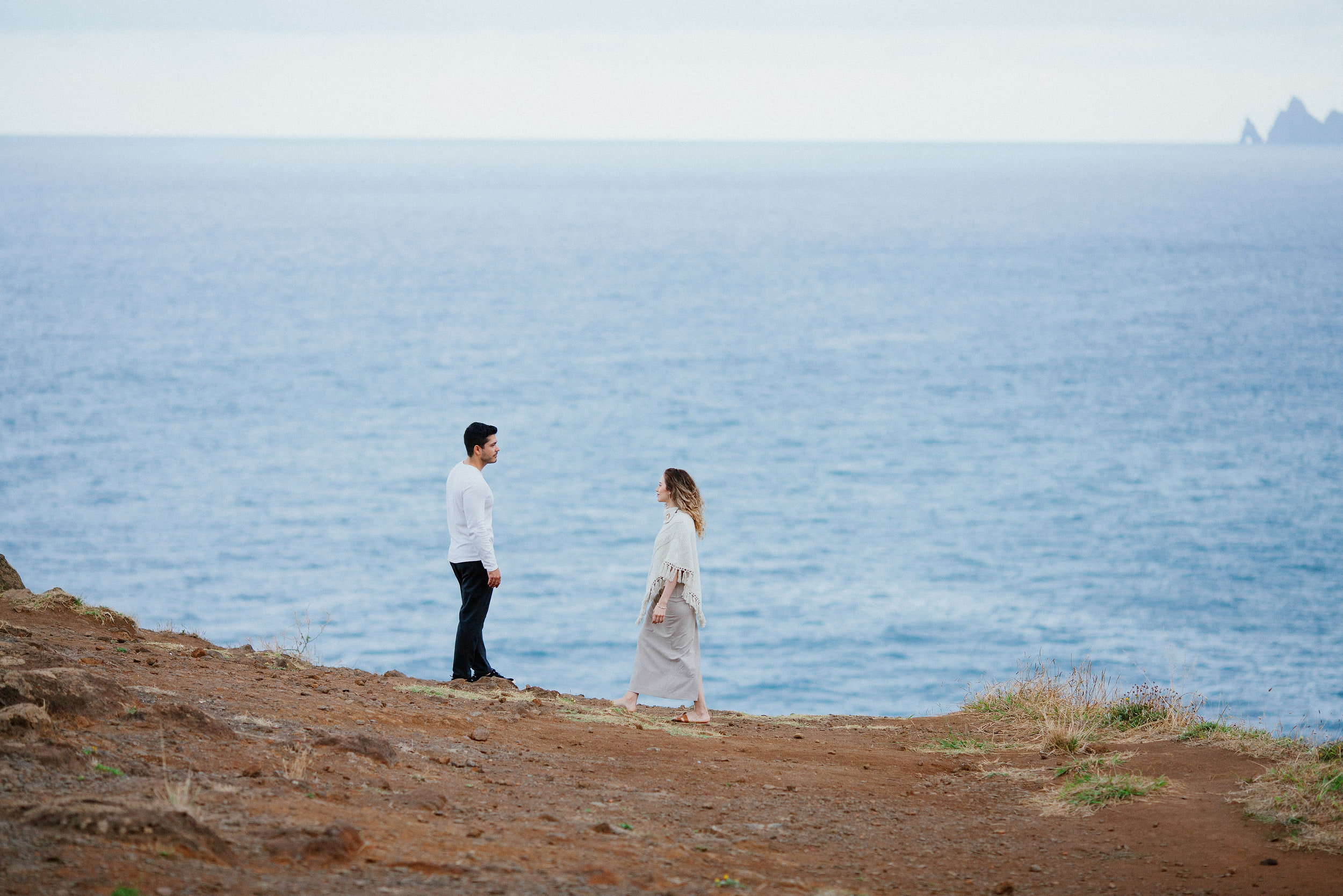 Lucas and Isabela facing each other on the bare clifftop, wide Atlantic behind them, Miradouro do Guindaste, Madeira