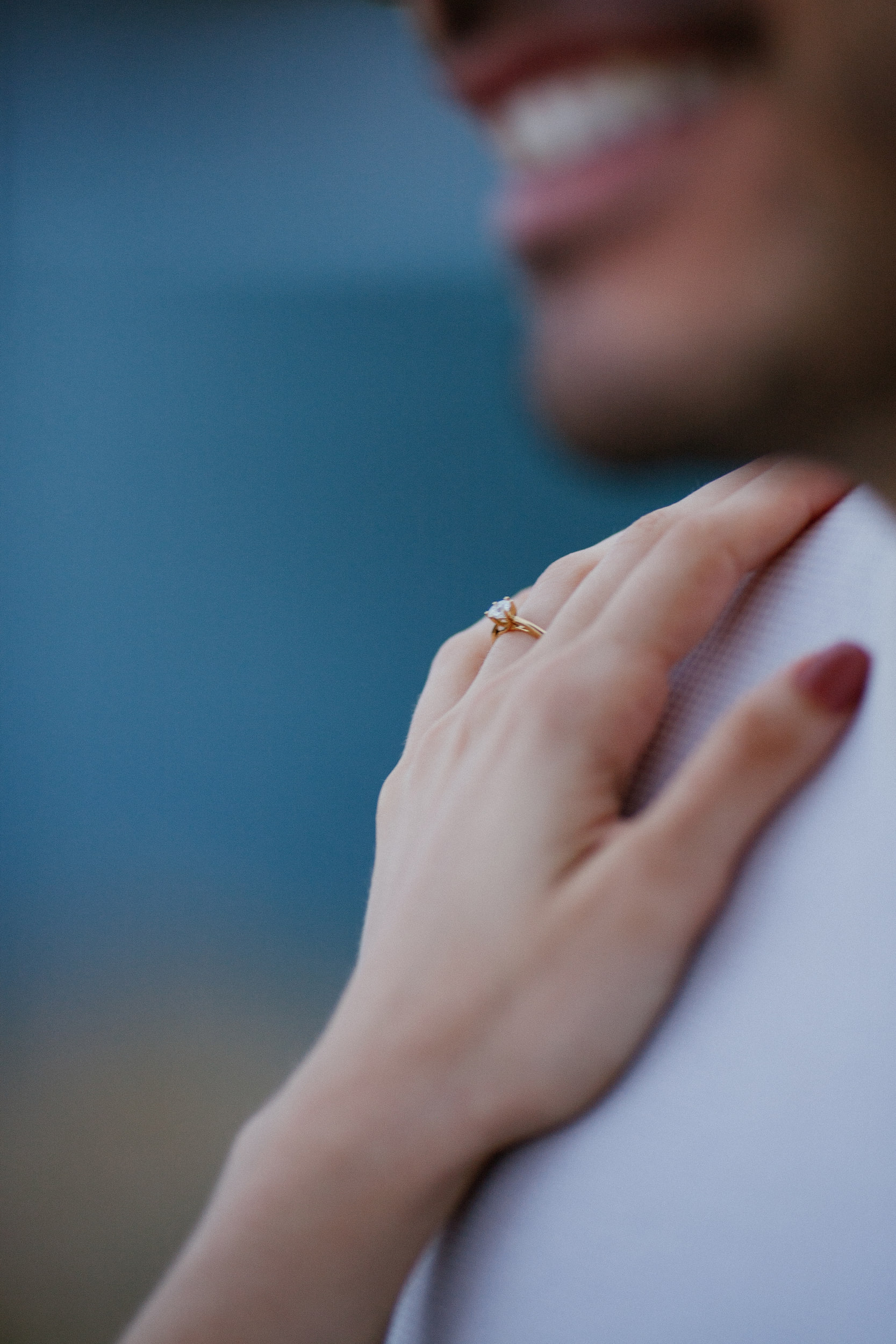 Isabela's hand with the ring on Lucas's shoulder, his smile blurred above, Miradouro do Guindaste, Madeira