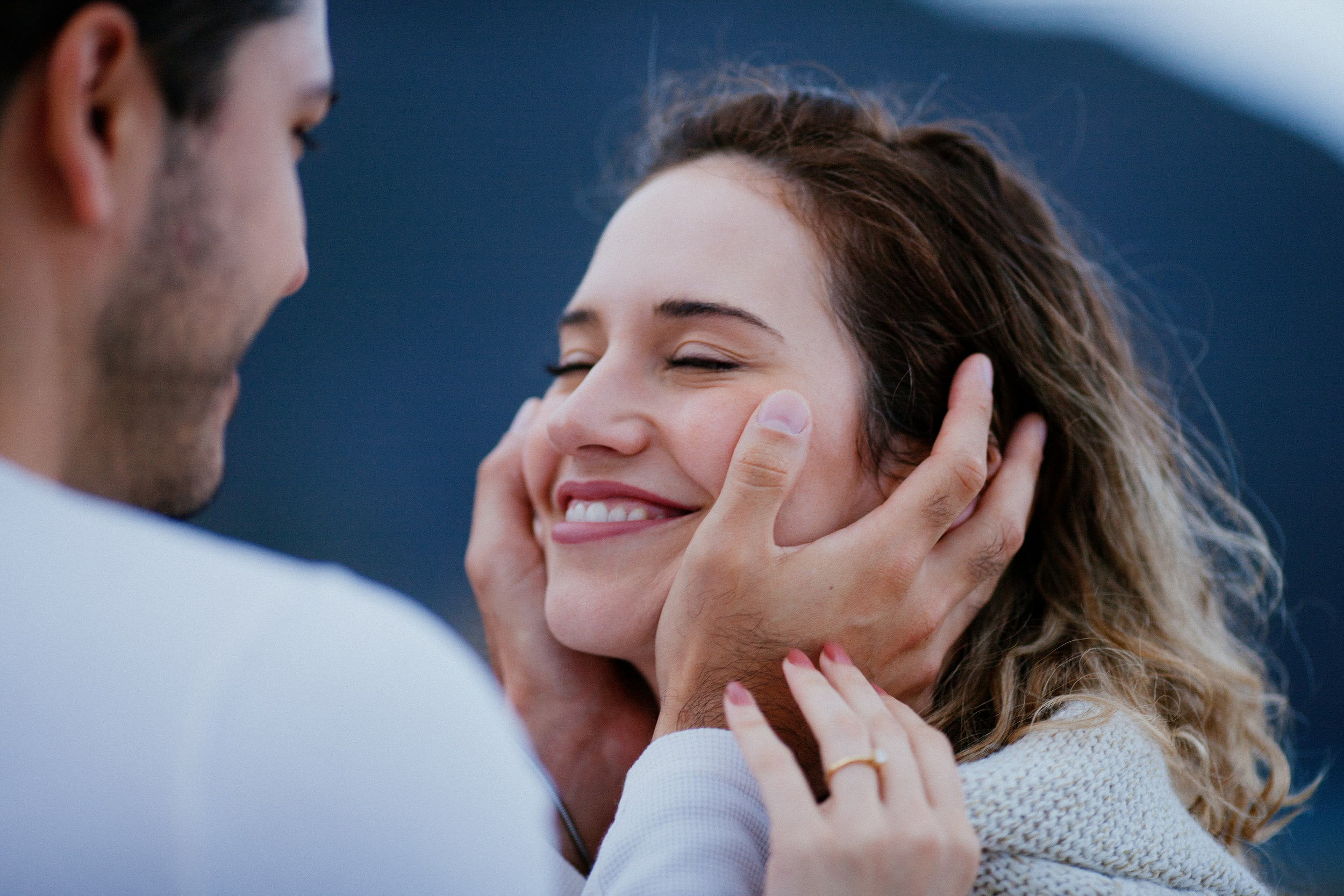 Isabela laughing with her eyes closed as Lucas holds her face, ring on her hand, Miradouro do Guindaste, Madeira