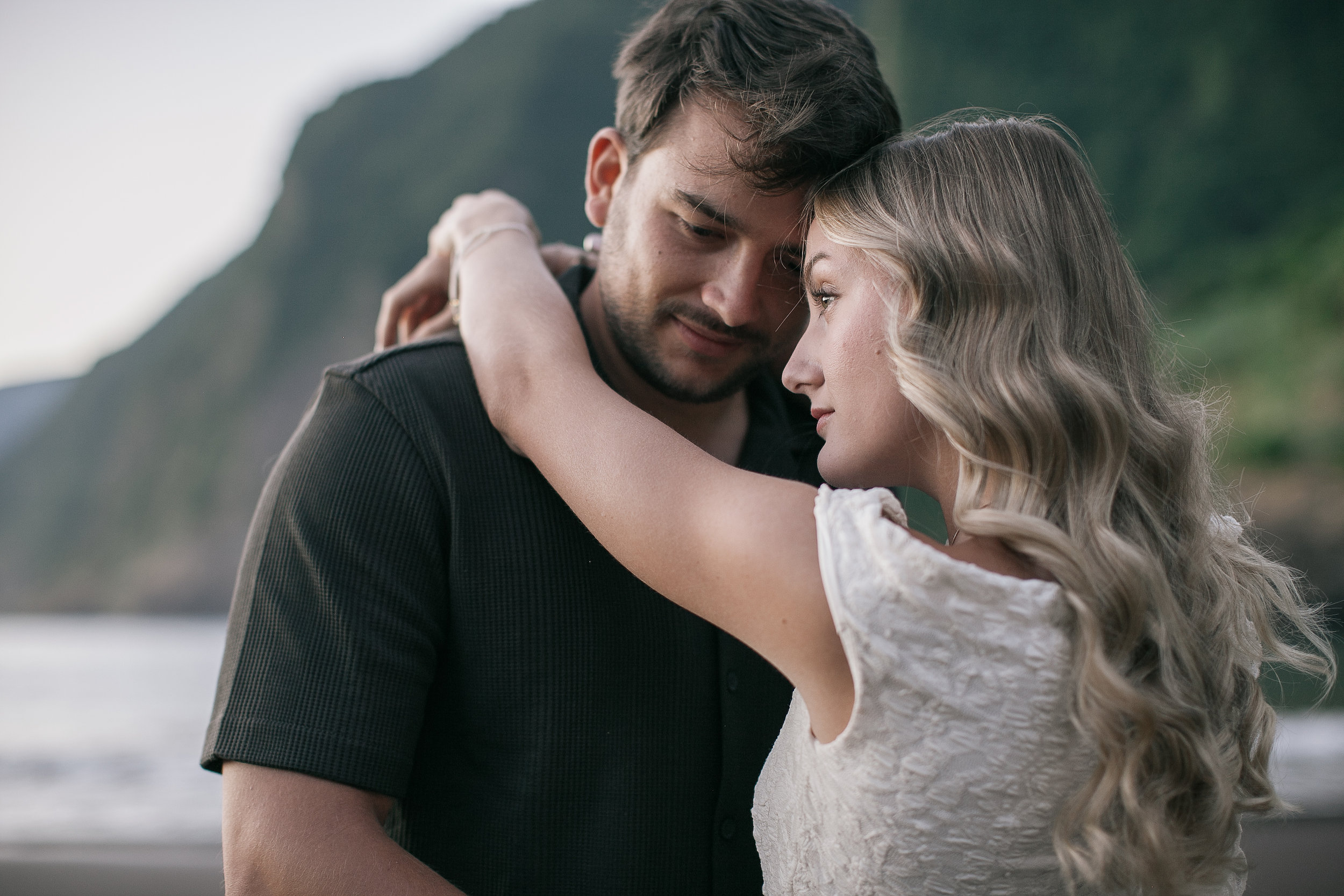 Her arm around his neck, foreheads close, green wall of Seixal behind, Madeira