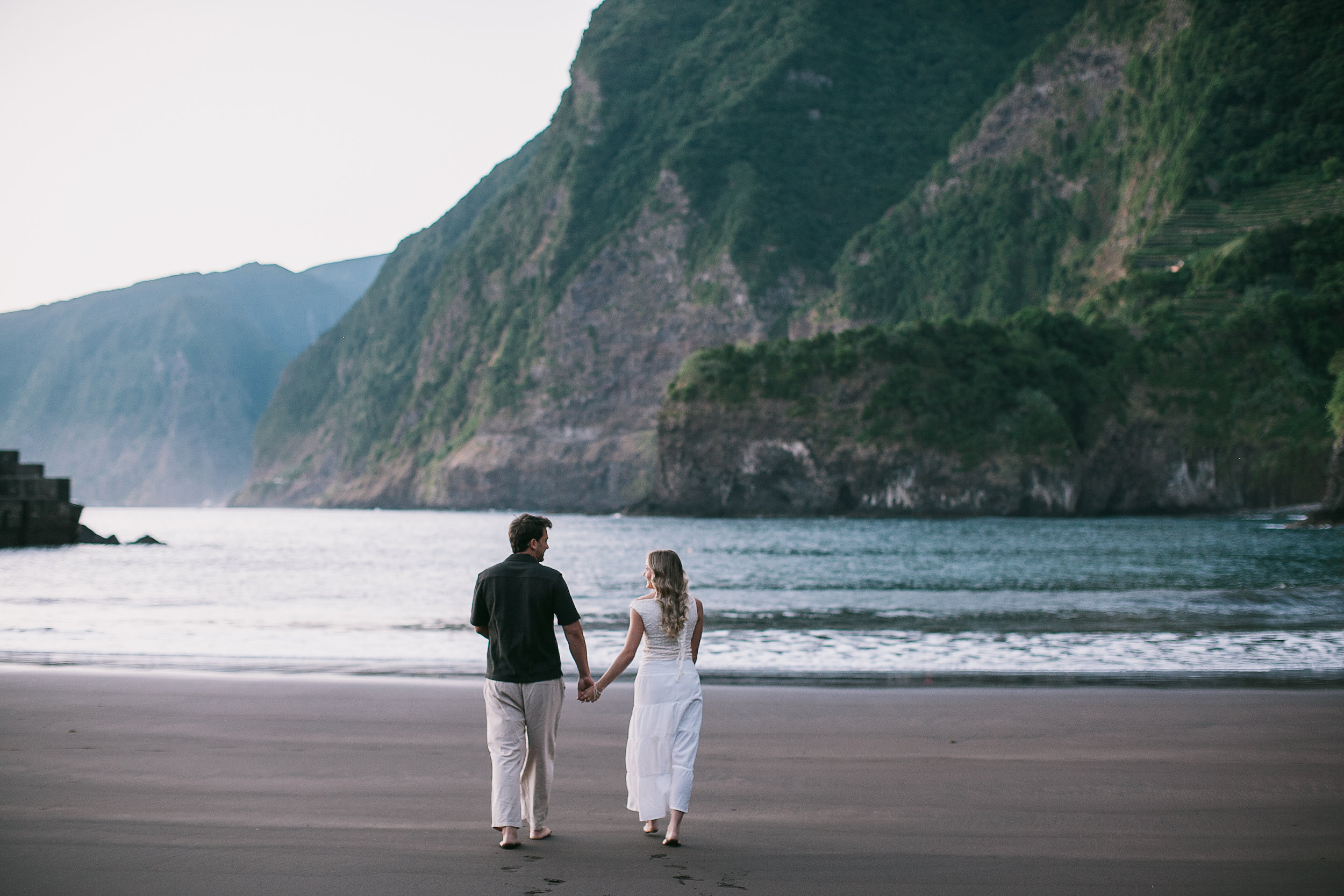 Hand in hand at the calm waterline, cliffs across the bay, Seixal, Madeira