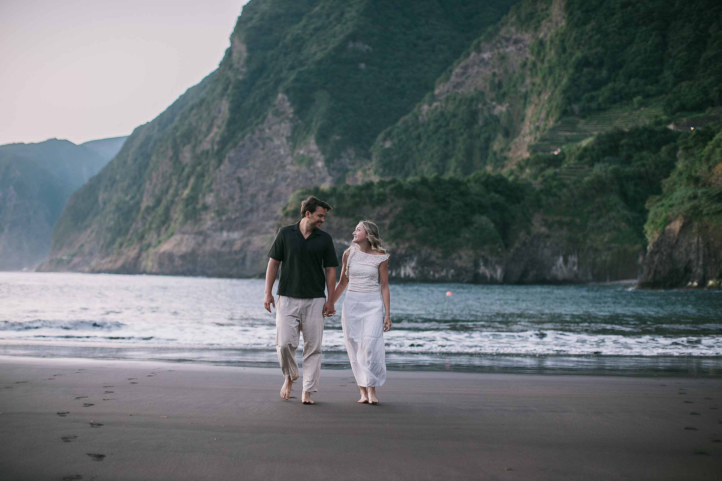 The couple small against the cliffs, walking the shore, Seixal, Madeira