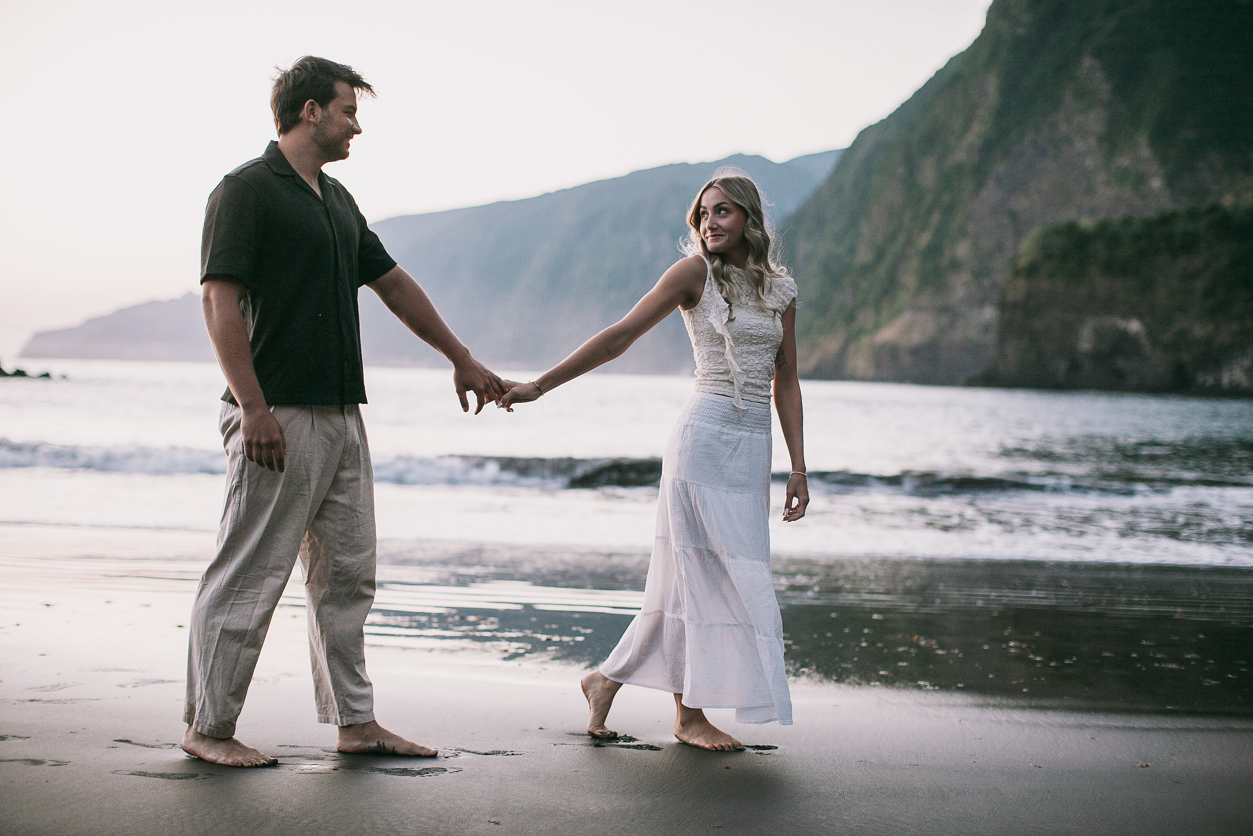 Leading each other along the waterline, white dress against dark sand, Seixal, Madeira