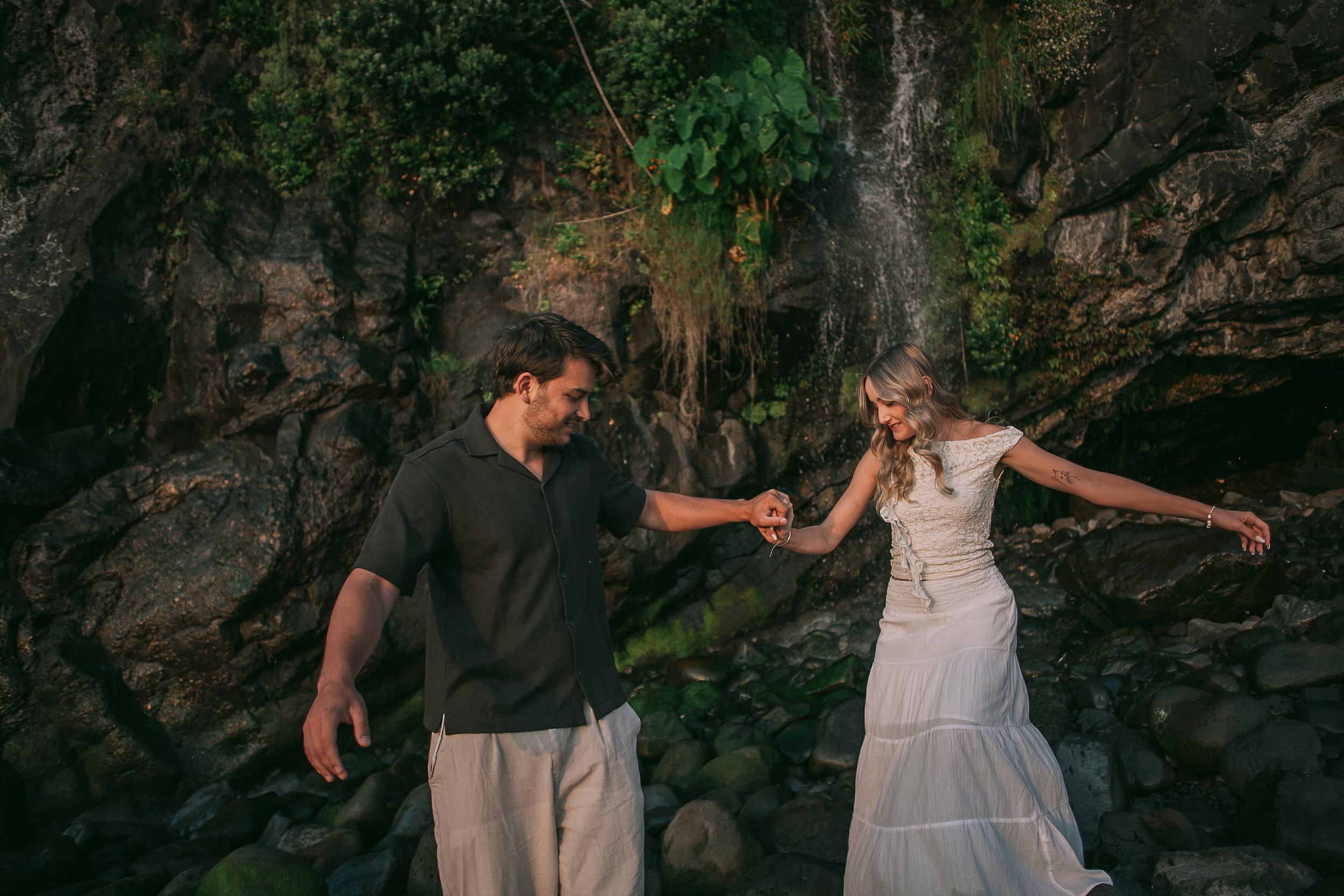 He steadies her across the wet rocks by the falls, Seixal, Madeira