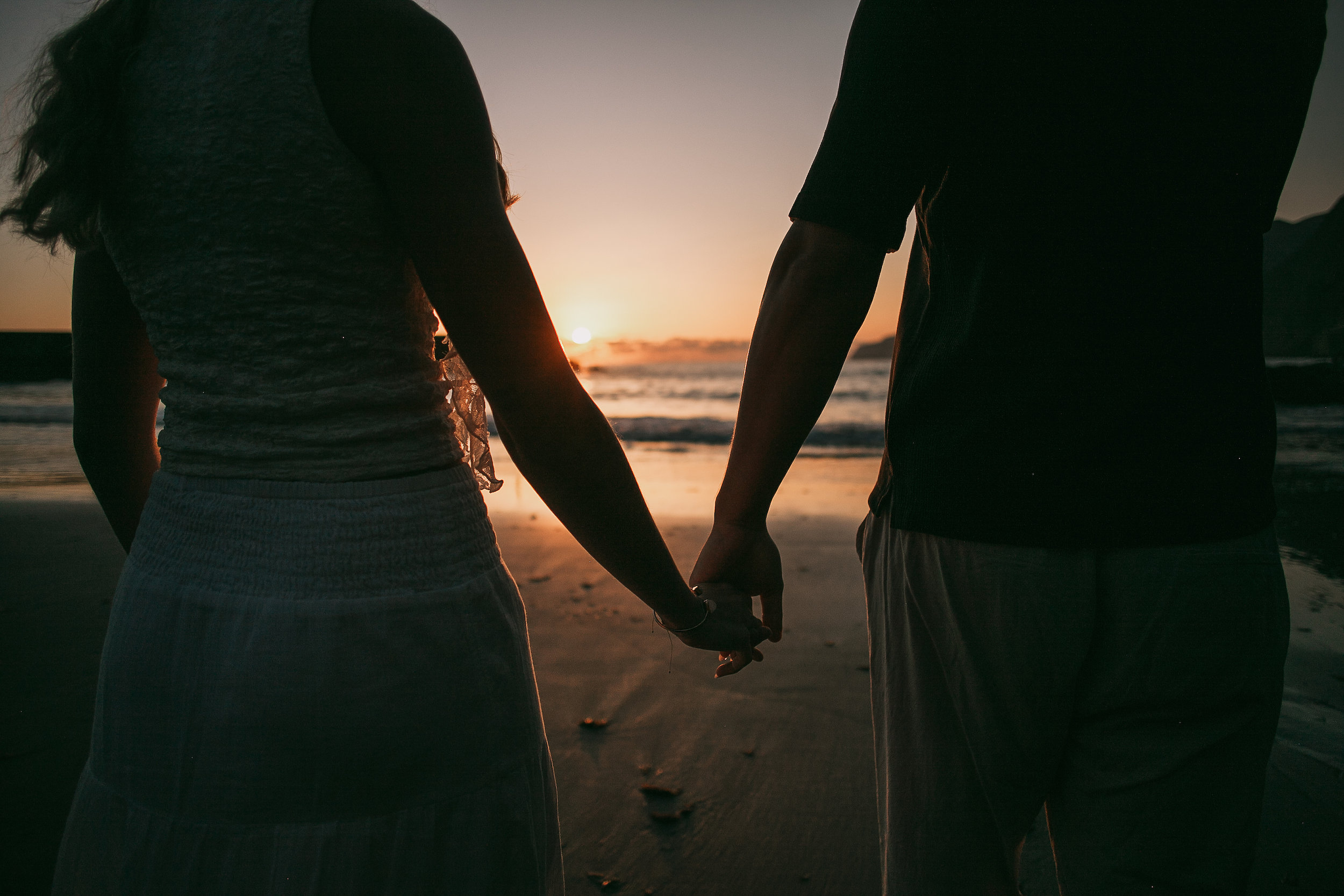 Their linked hands in silhouette against the sunset, Seixal Beach, Madeira