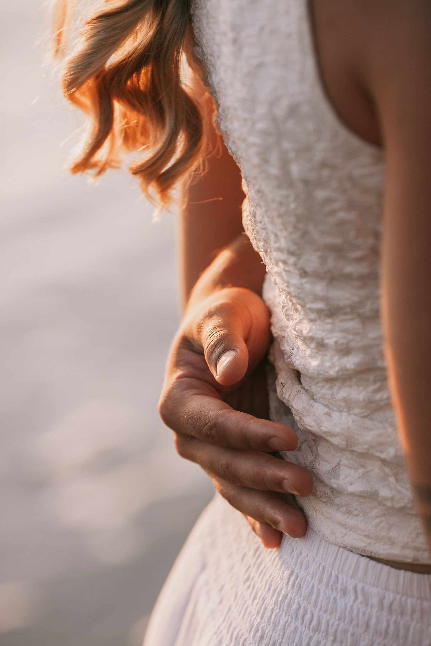 His hand at her waist over the white dress, detail at sunset, Seixal, Madeira