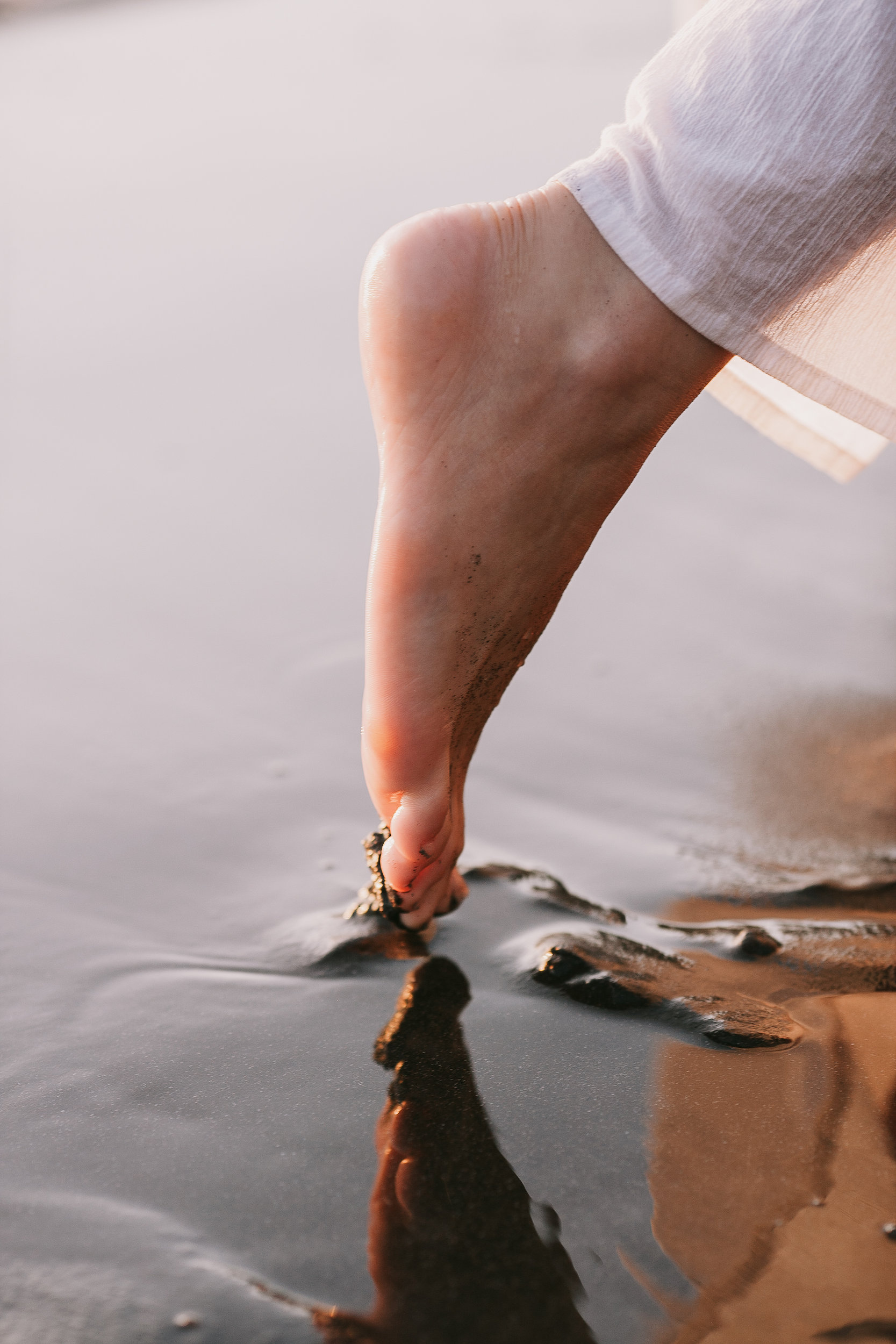 Her bare foot touching the wet sand, golden light, Seixal Beach, Madeira