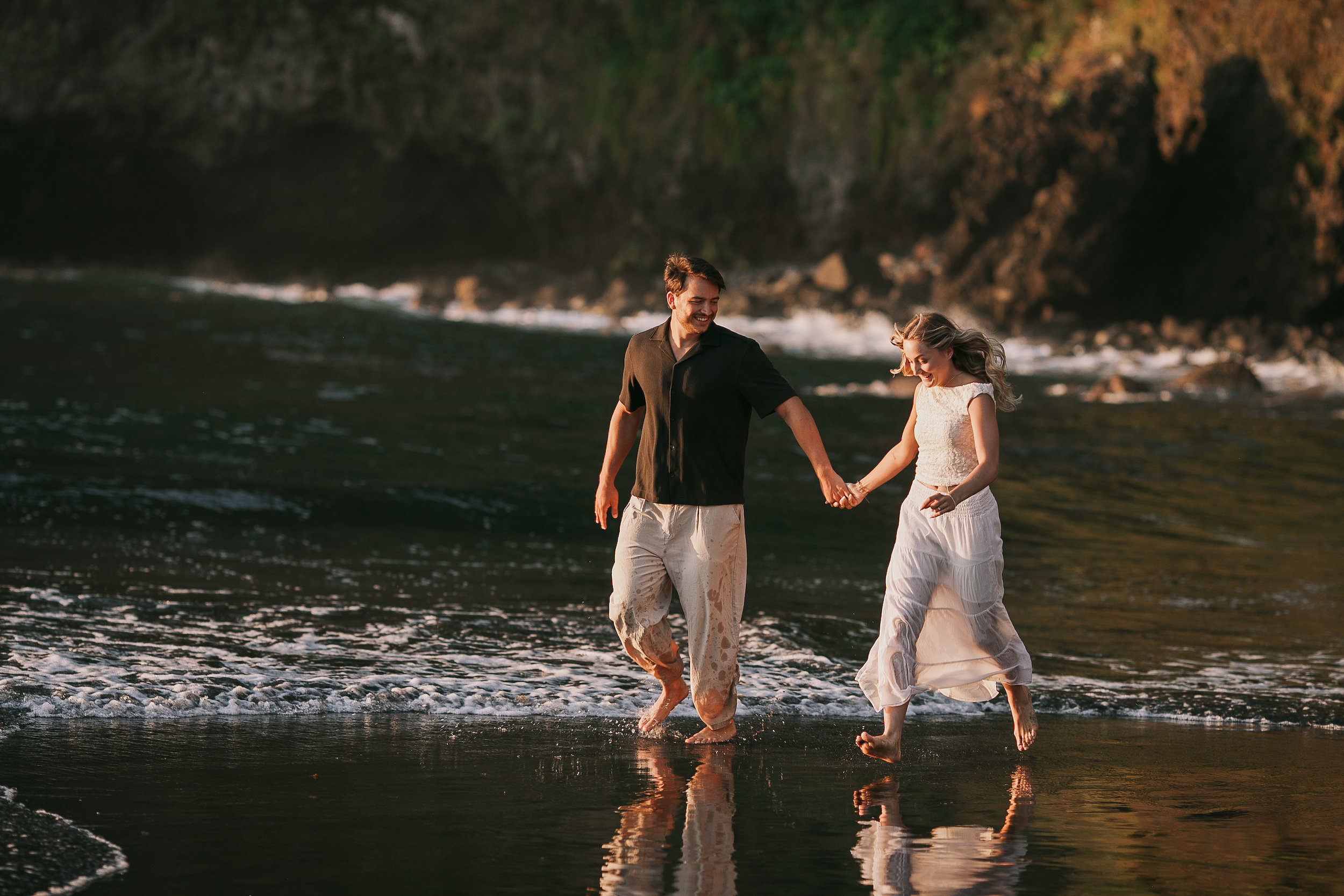 Wading hand in hand past the dark rocks, warm light on the water, Seixal, Madeira