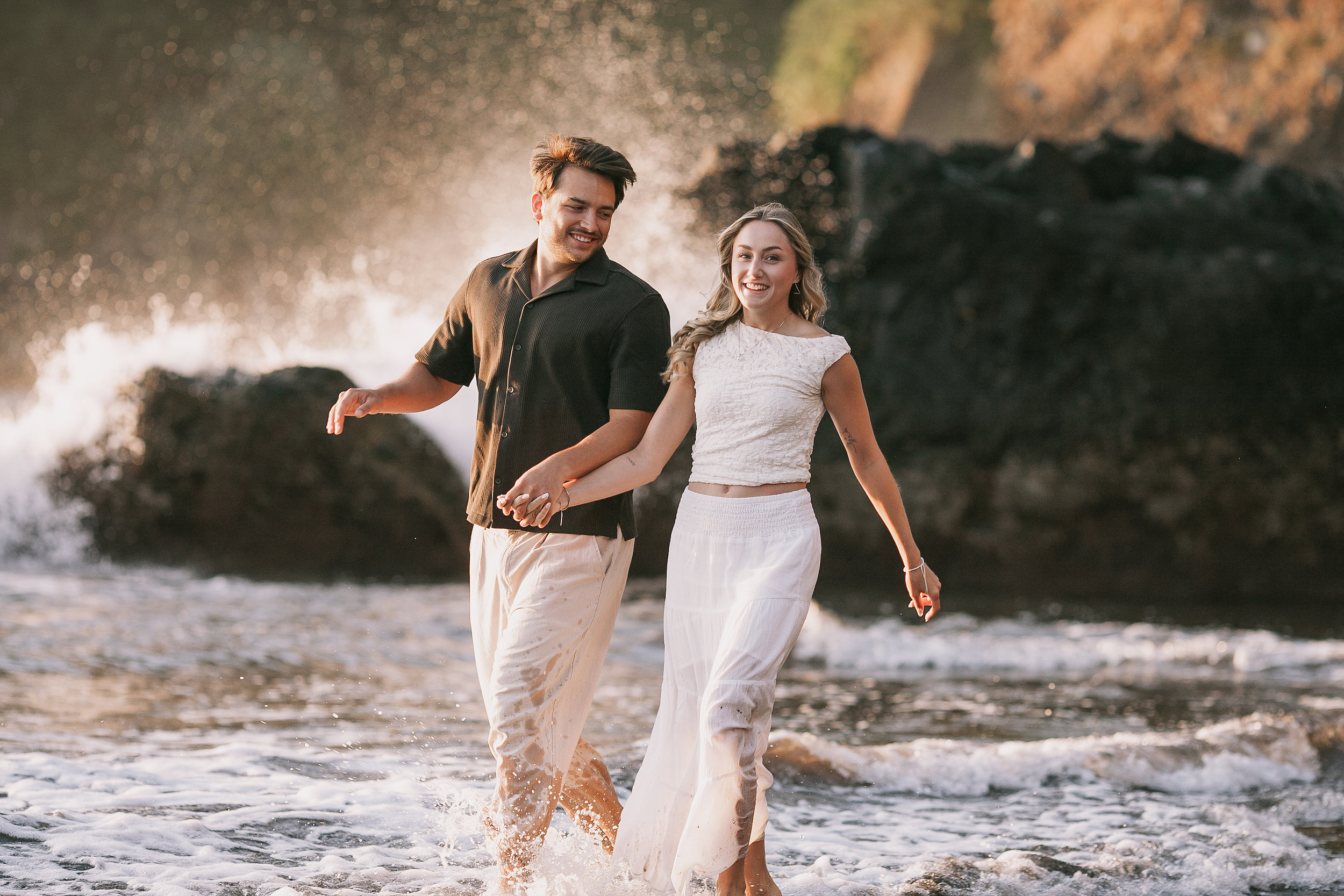 Laughing as surf bursts against the sea stack behind them, Seixal Beach, Madeira