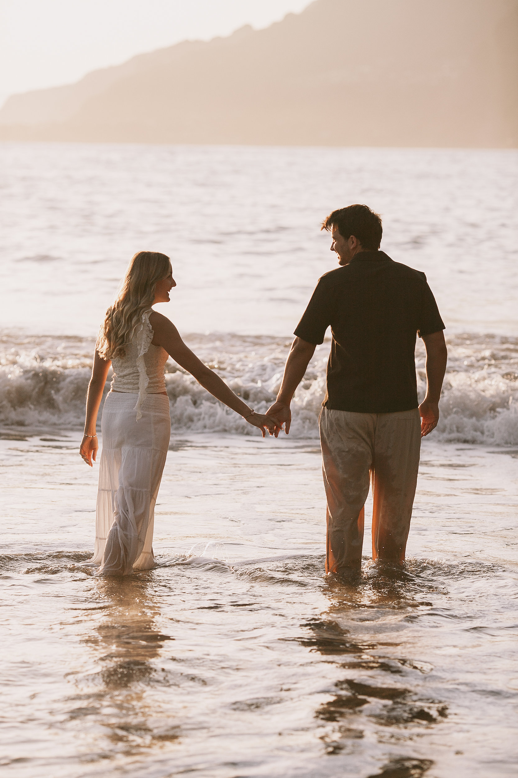 Standing in the sea holding hands, sun on the horizon, Seixal Beach, Madeira