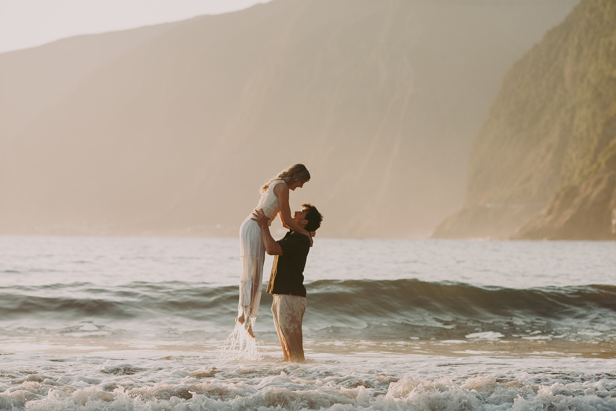 He lifts her above the waves, sunset behind, Seixal, Madeira