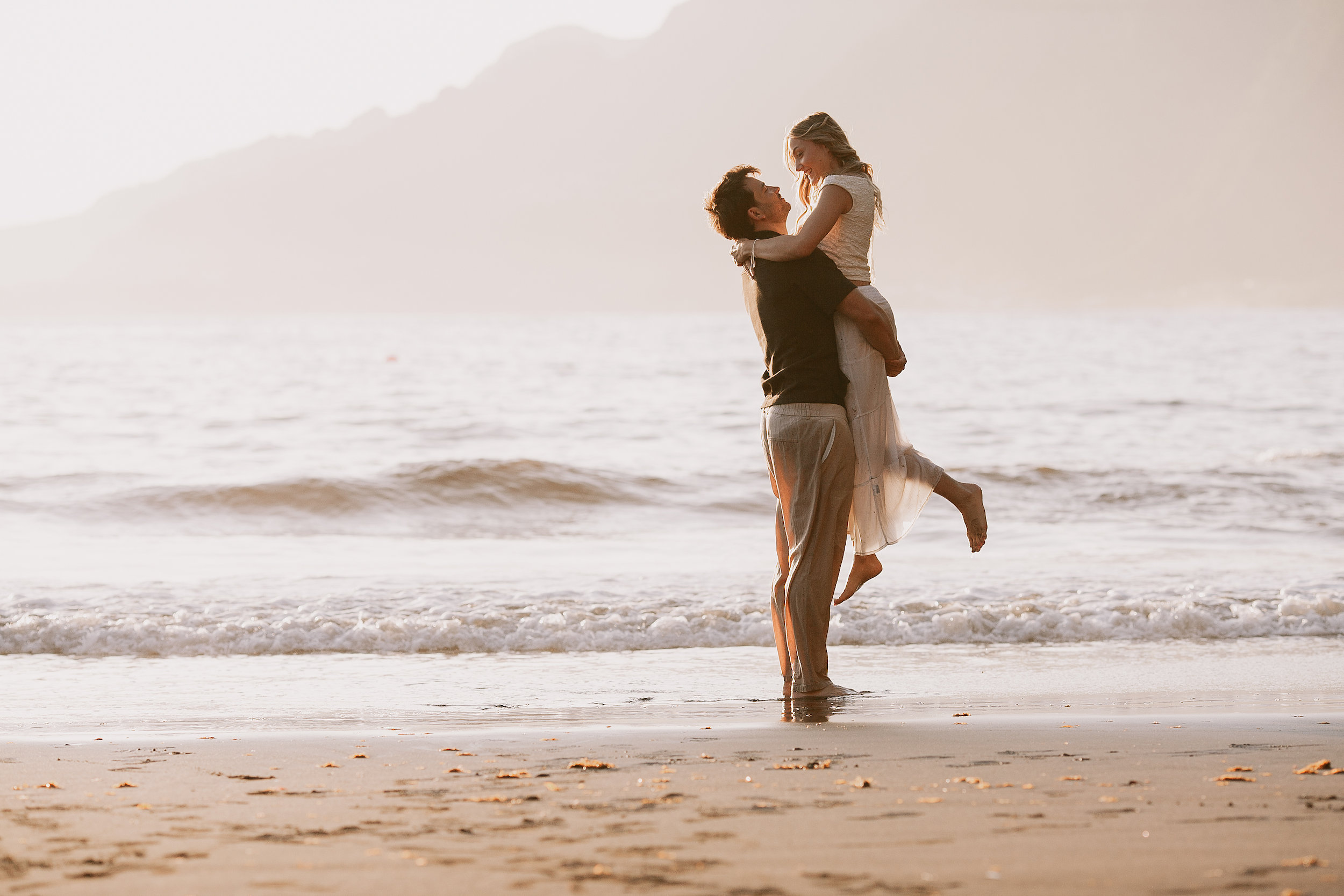 He lifts her at the shoreline, her feet off the sand, Seixal, Madeira