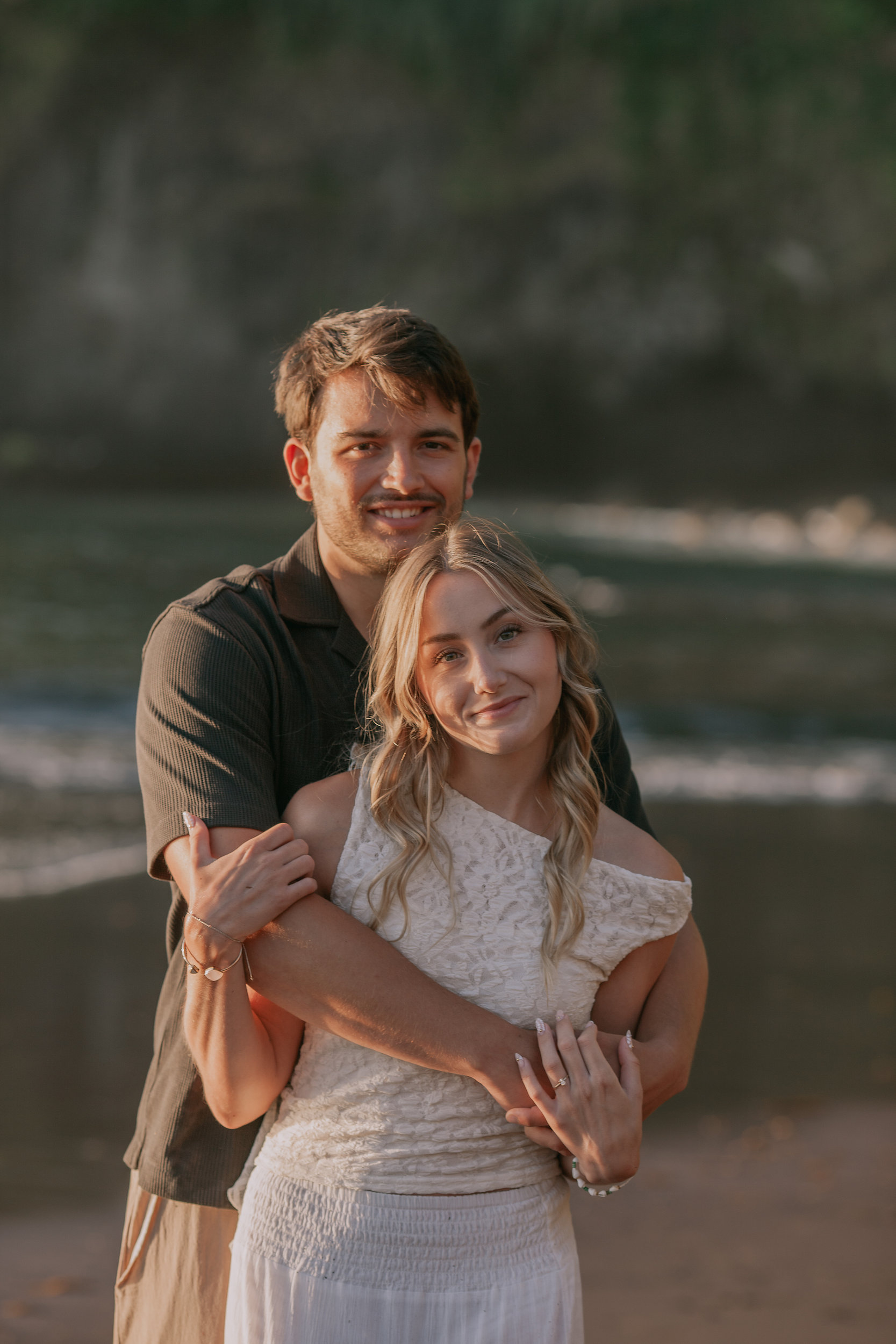 He wraps her from behind, both smiling at the camera, Seixal Beach, Madeira