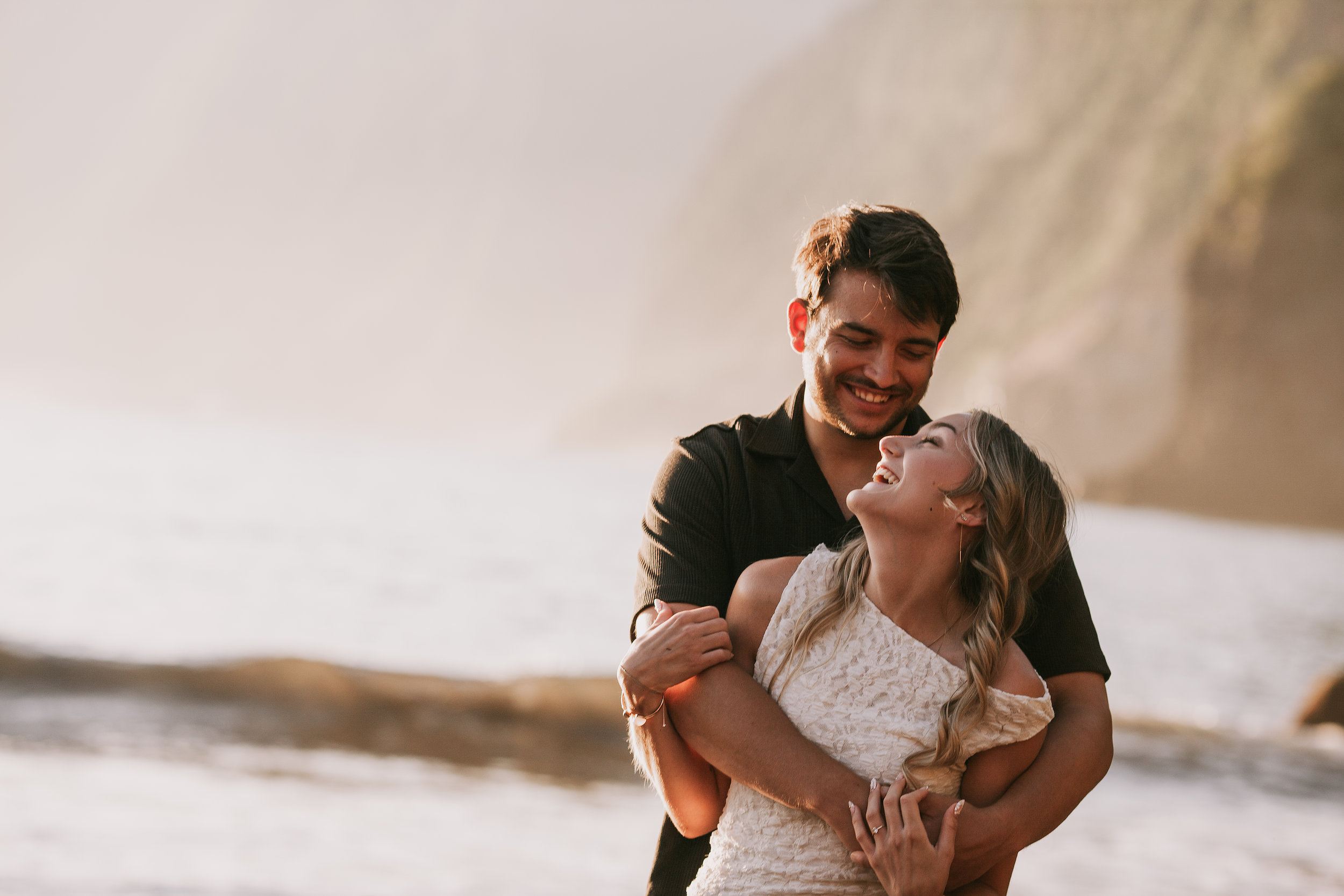 Hugging her from behind laughing by the dark rocks, Seixal, Madeira