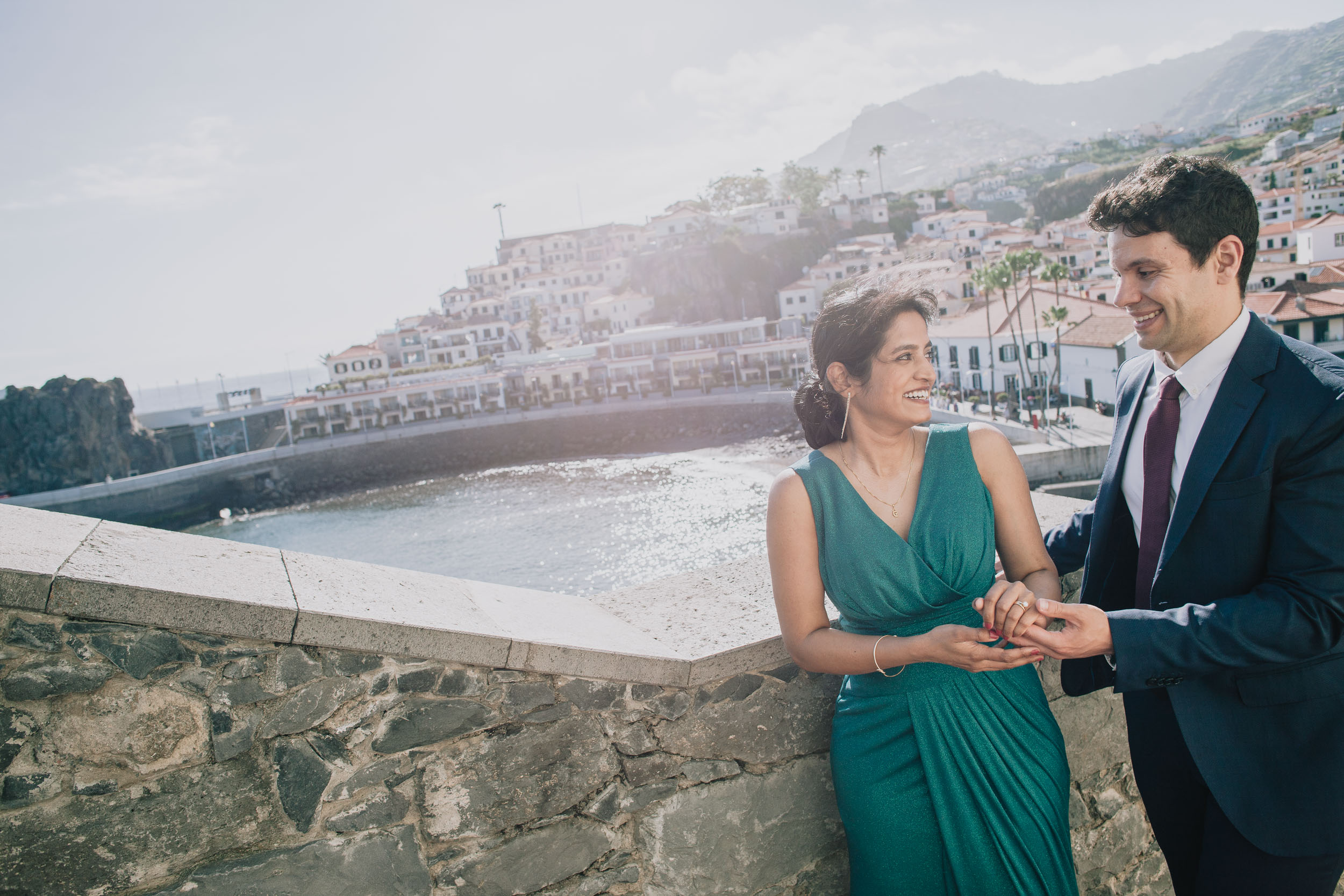 He takes her hand at the harbour wall, both smiling, the terraced white houses of the village rising behind, Camara de Lobos, Madeira