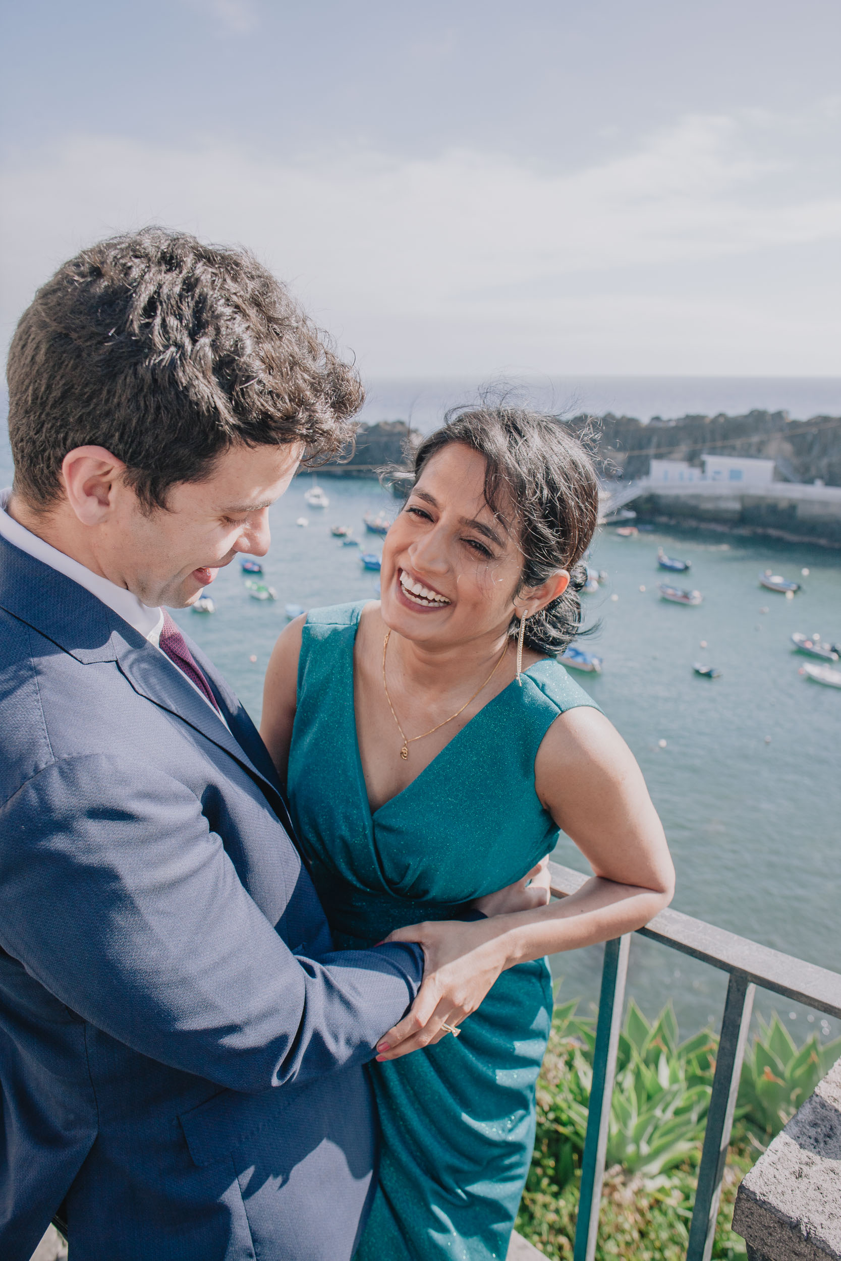 Bride laughing as she looks at the groom by a railing above Câmara de Lobos harbour, Madeira