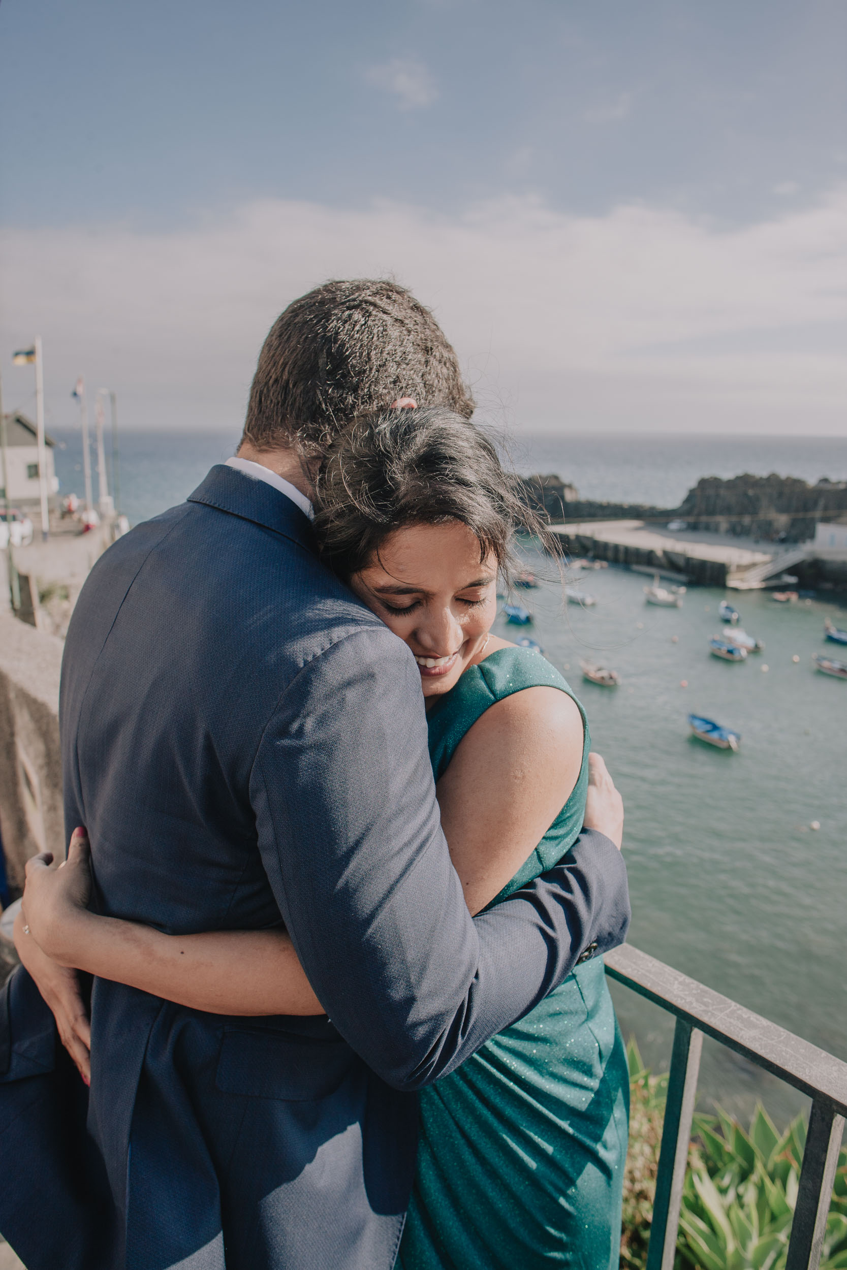 Bride pressed against the groom's chest with her eyes closed and smiling, the harbour and its boats behind, Câmara de Lobos, Madeira