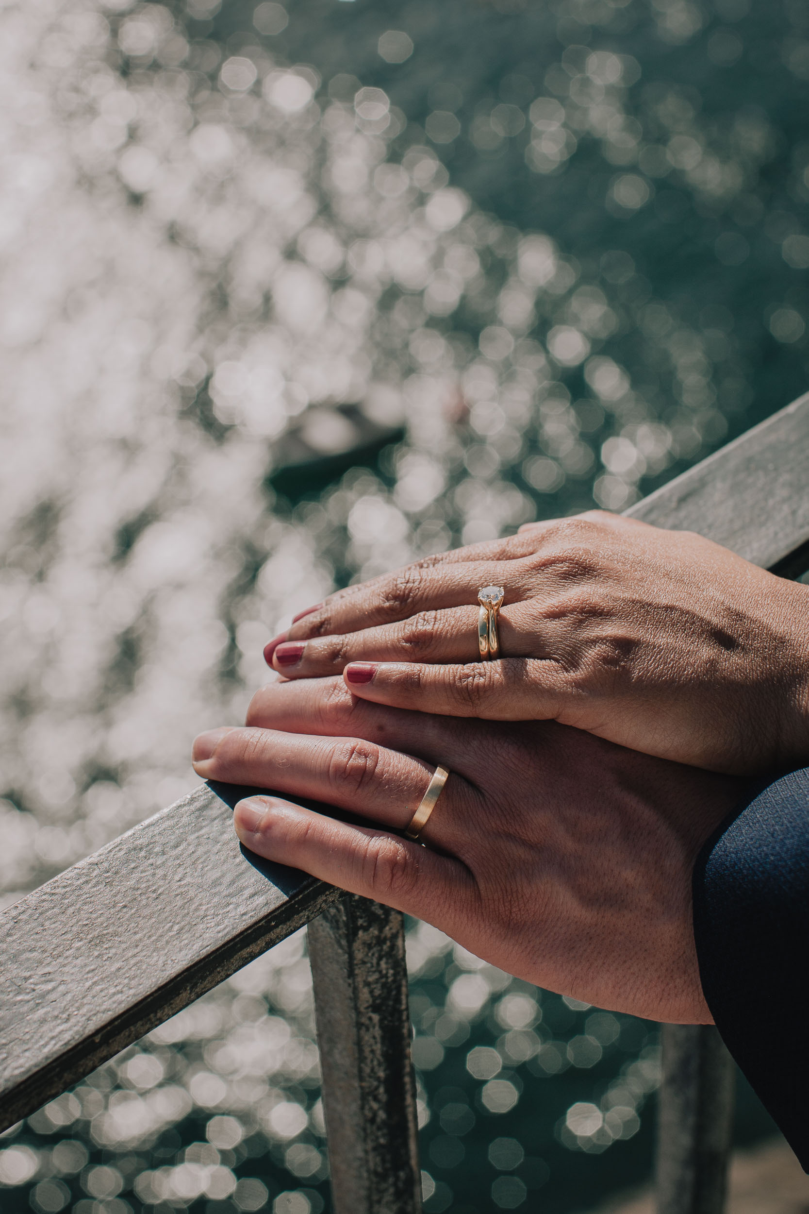 Detail. Her hand with the engagement ring resting on his, both on the weathered railing above the sunlit water, Camara de Lobos, Madeira