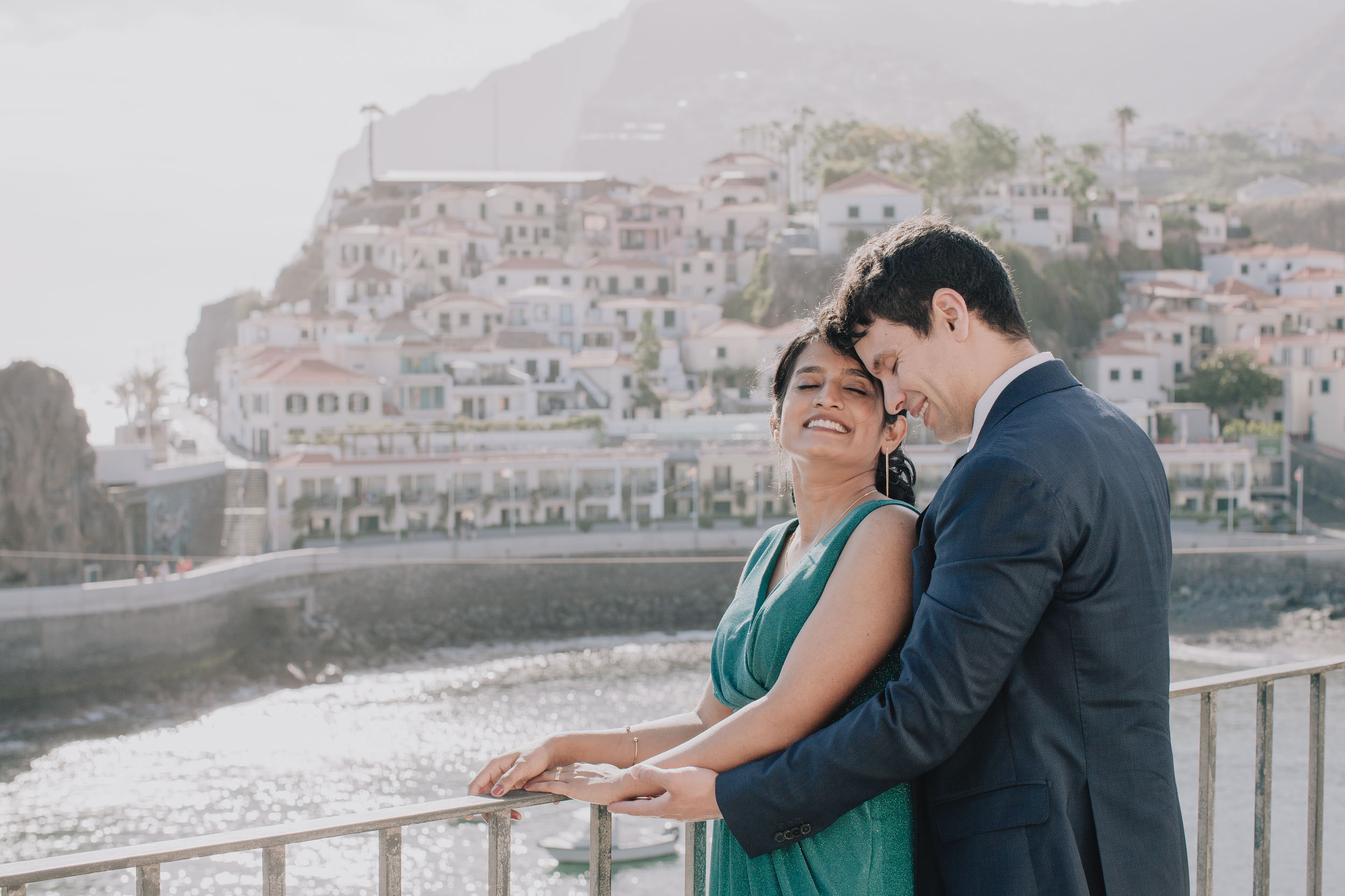 Couple embracing on a terrace, foreheads touching, the houses of Câmara de Lobos rising up the hillside behind, Madeira