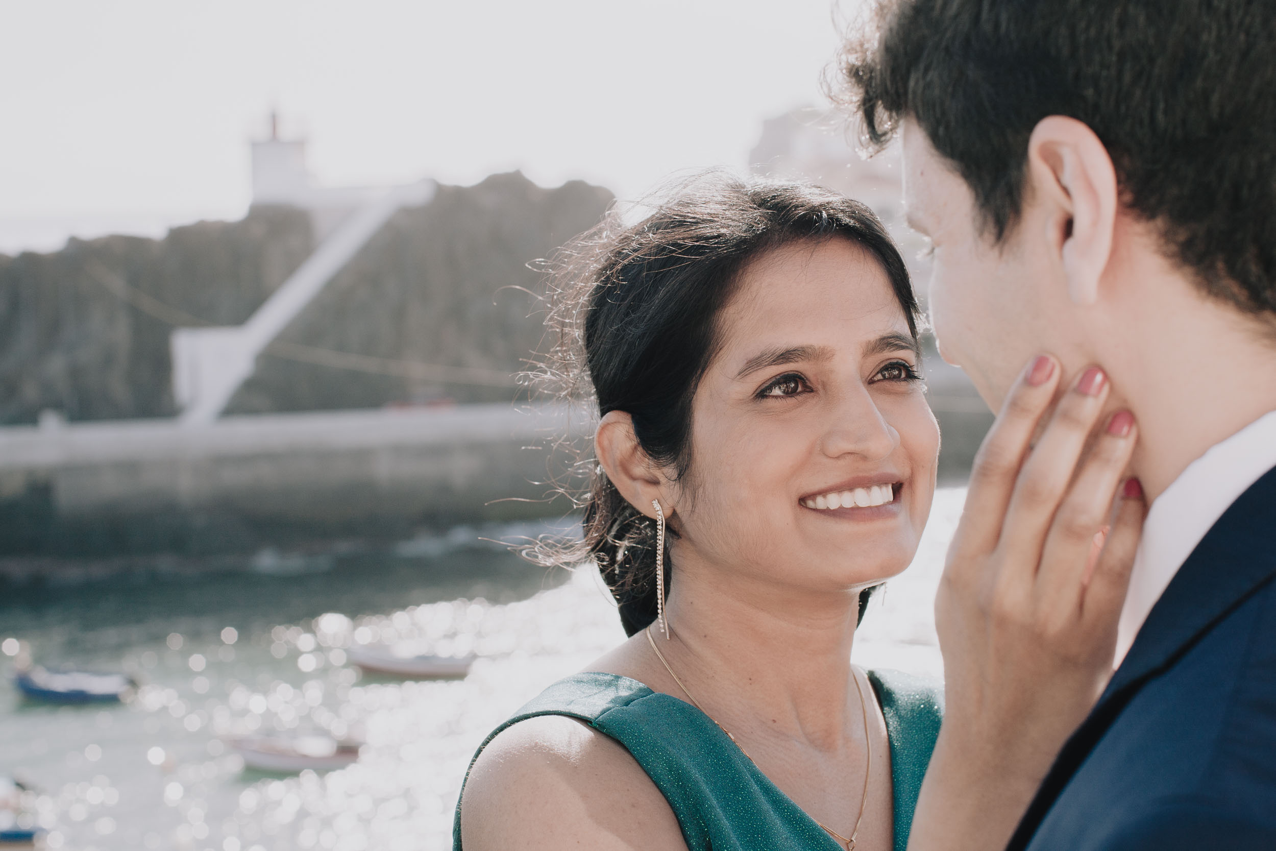 Bride resting her hand on the groom's cheek, looking at him tenderly, the harbour soft behind, Câmara de Lobos, Madeira