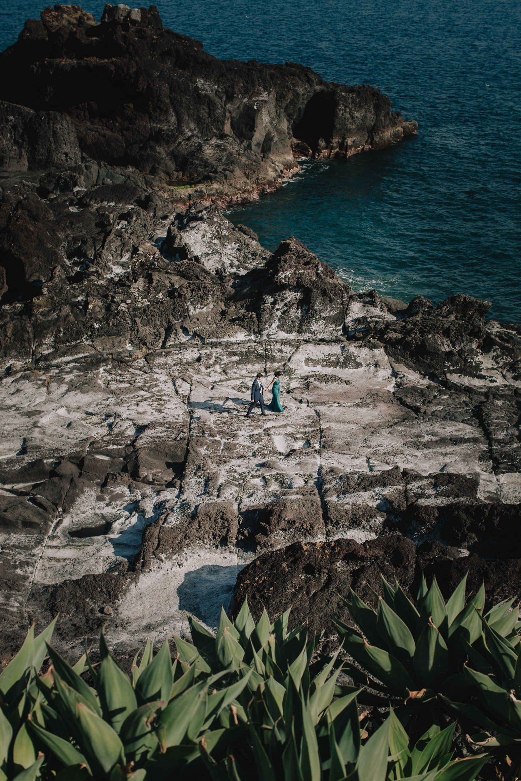 Couple standing small among dark volcanic rocks above the Atlantic at Câmara de Lobos, Madeira