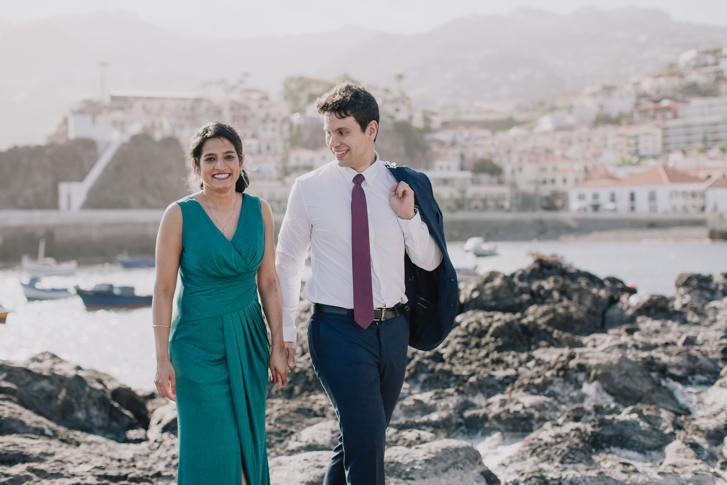 Walking hand in hand over the black lava shelf, his jacket over his shoulder, the harbour behind, Camara de Lobos, Madeira