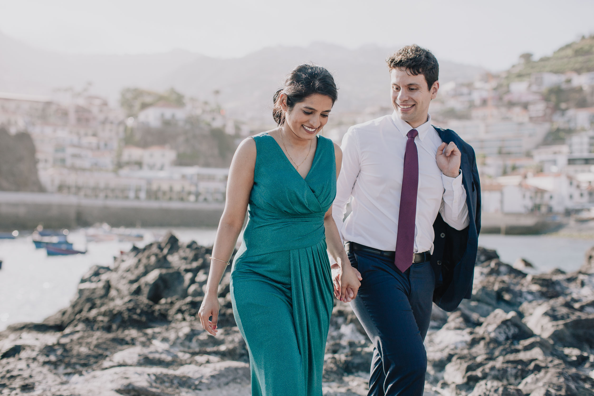 Couple laughing as they walk across the volcanic rocks, Câmara de Lobos village behind, Madeira