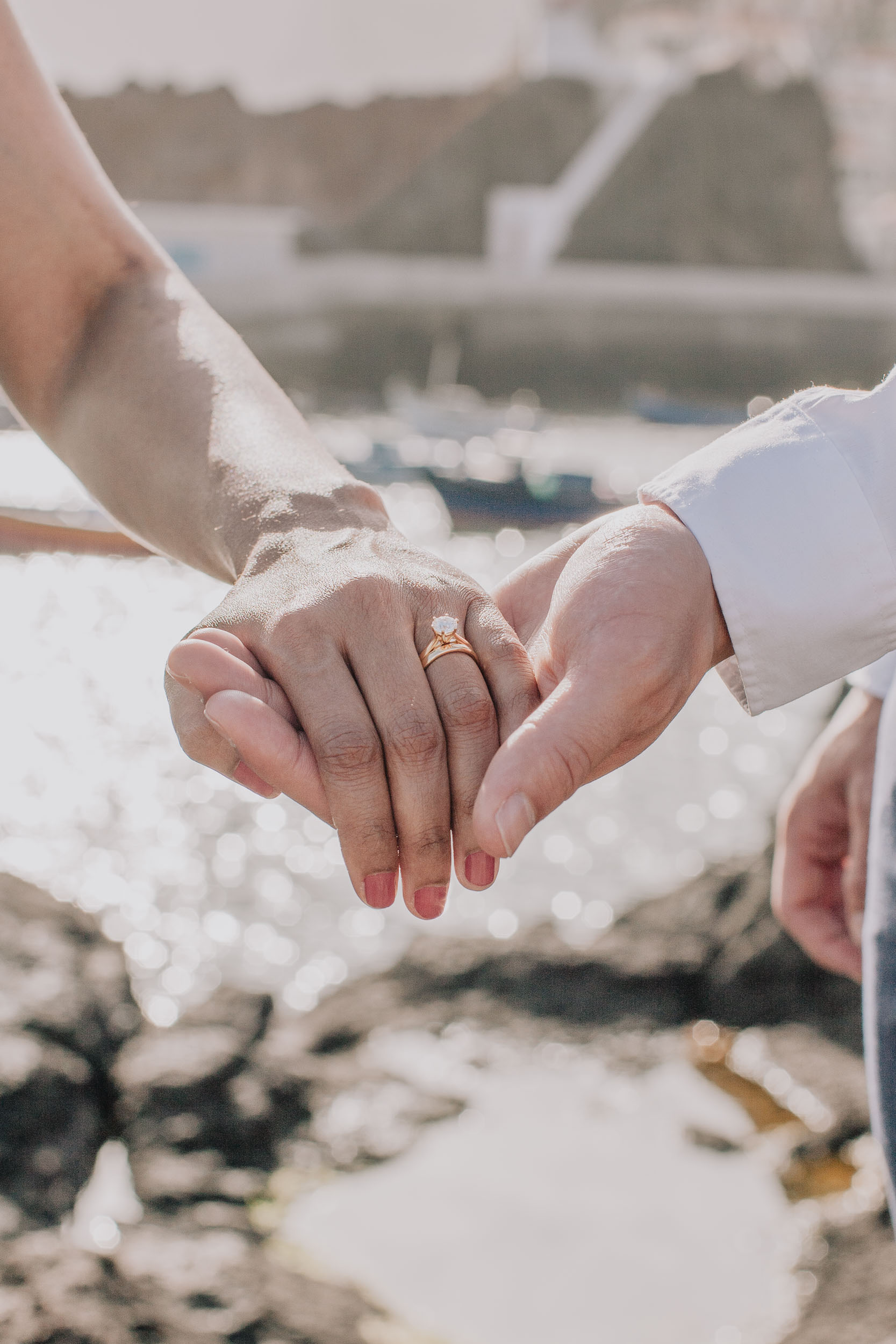 Close detail of the couple's clasped hands with the bride's diamond ring, the harbour soft behind, Câmara de Lobos, Madeira