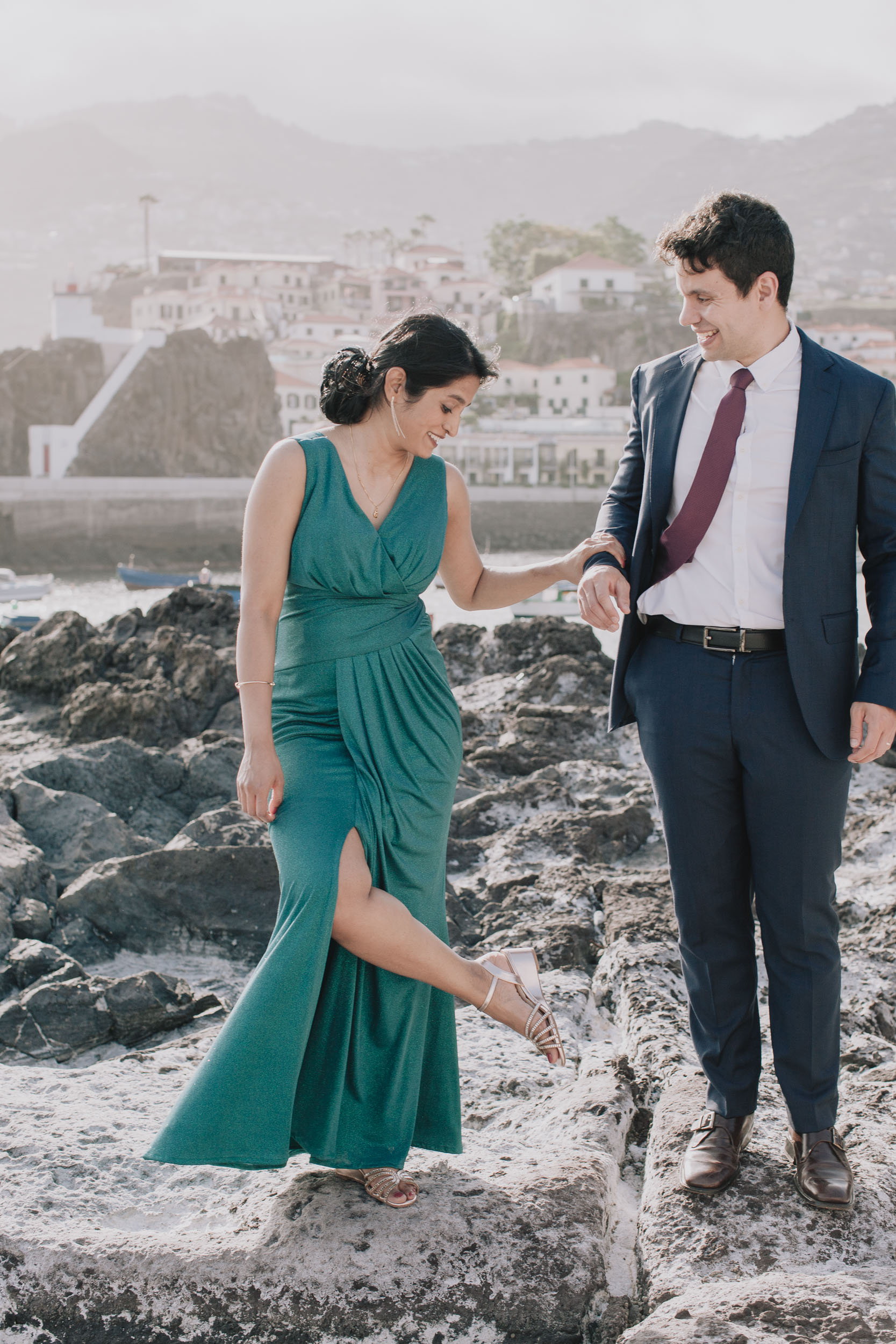 Vertical frame. She steadies herself on his arm and steps down off the rock, both laughing, Camara de Lobos, Madeira
