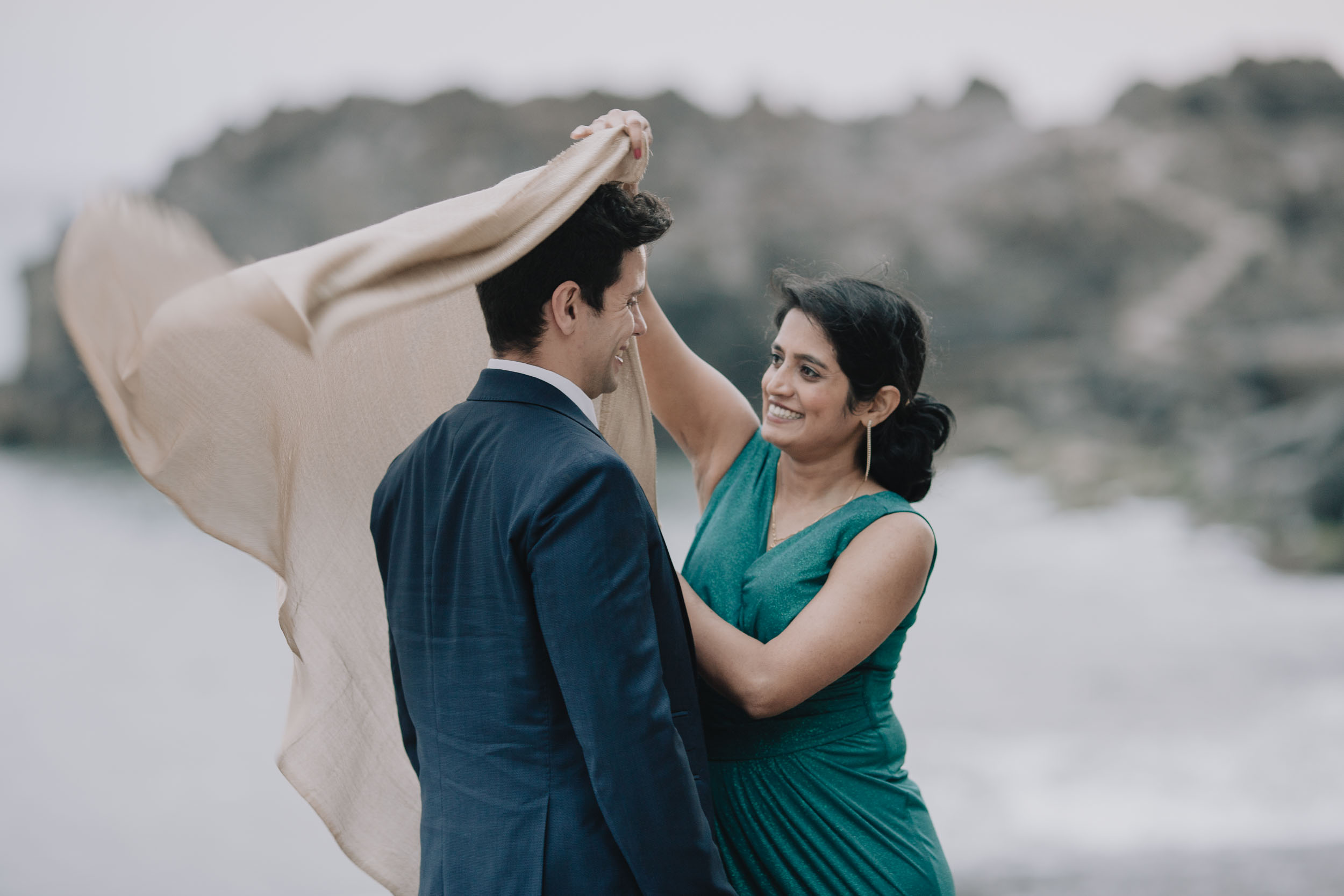 Couple holding a scarf that lifts in the wind above them, the bride laughing, the Atlantic behind, Câmara de Lobos, Madeira