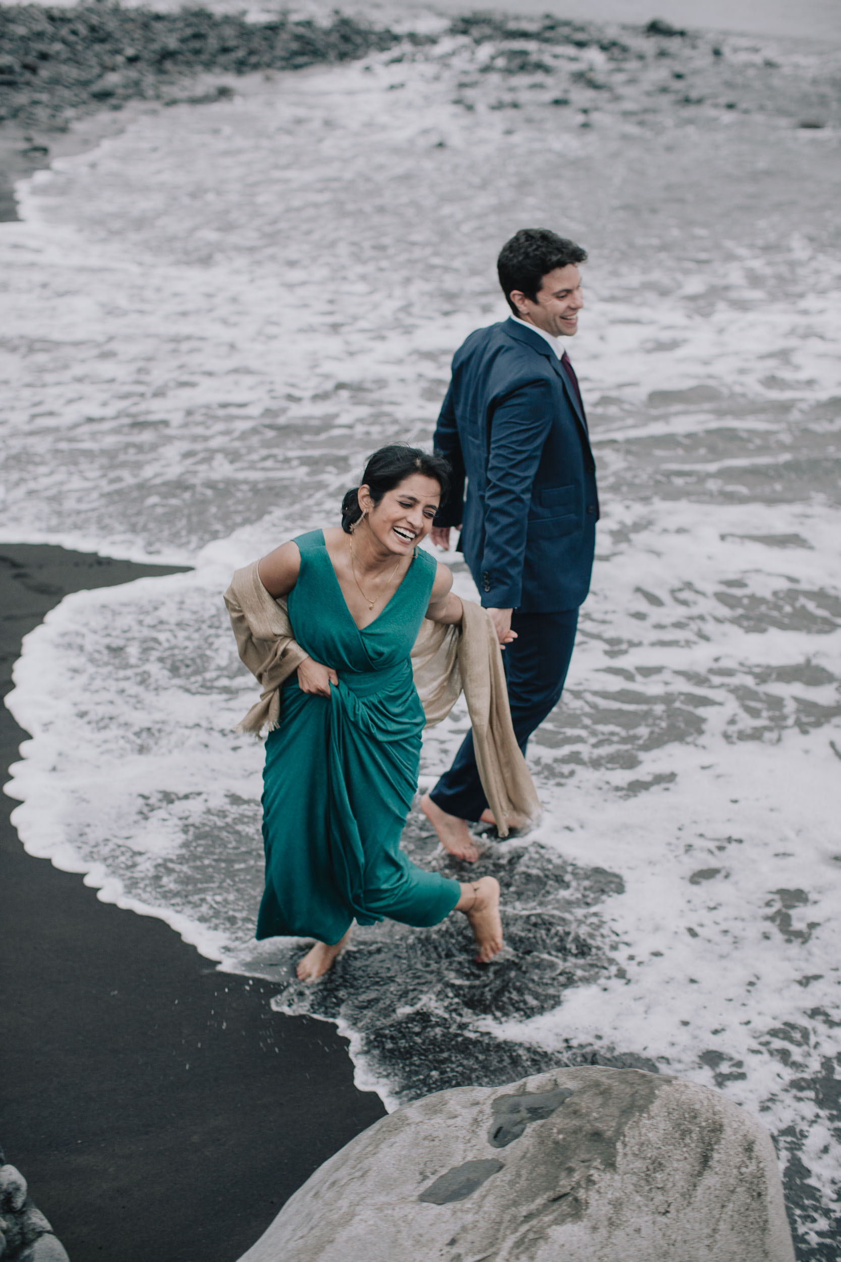Couple walking barefoot through the surf on the dark beach, the bride laughing, Câmara de Lobos, Madeira