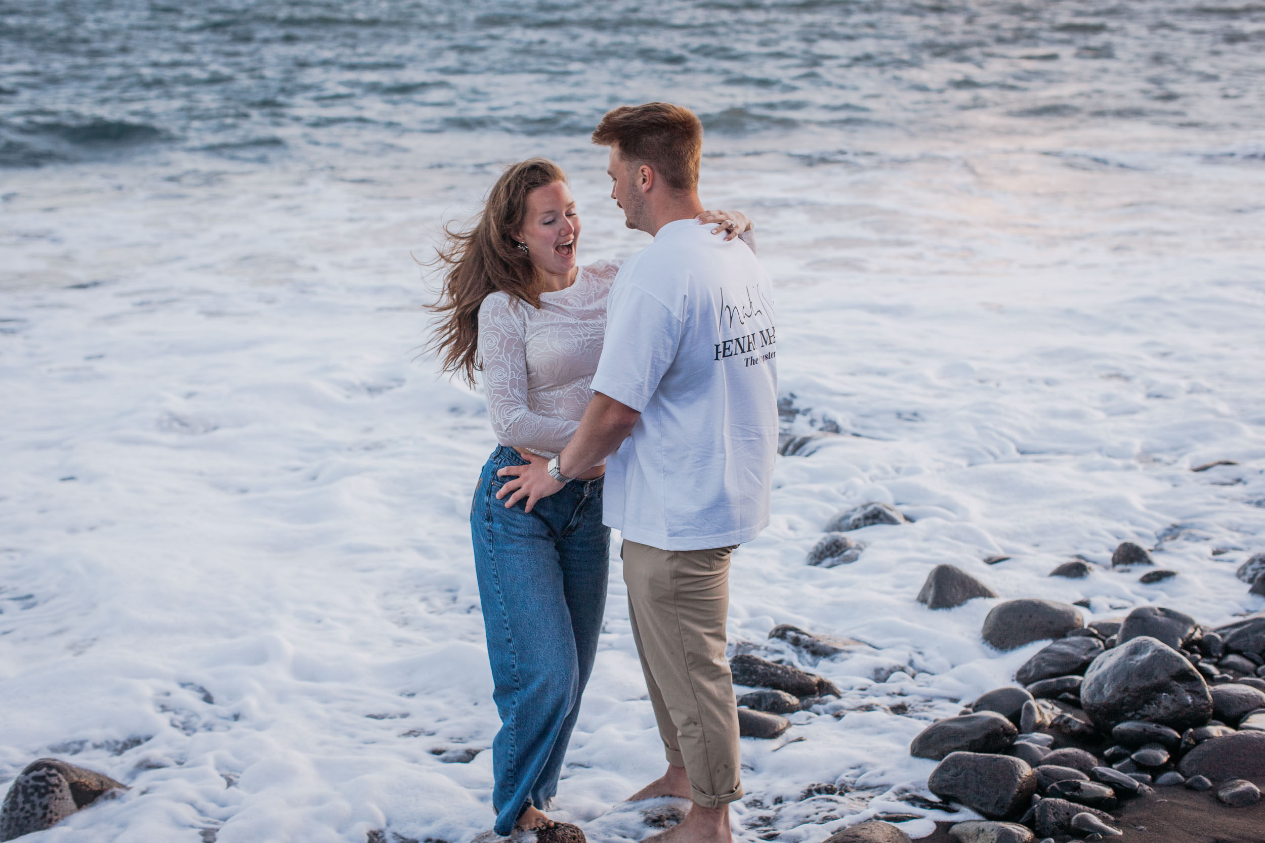 Standing ankle deep in the foam, she laughs with her head back and her hand on his chest, Praia Formosa, Madeira