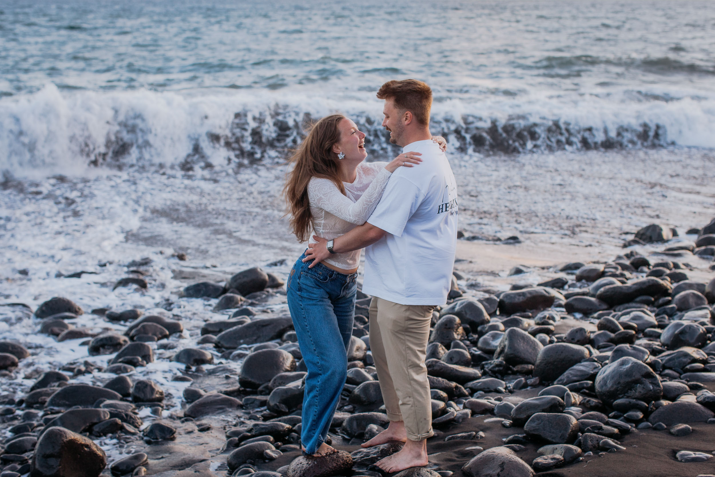 Rylie and Abby in a close embrace as a wave rolls in behind, last light on the cliffs at Praia Formosa, Funchal, Madeira