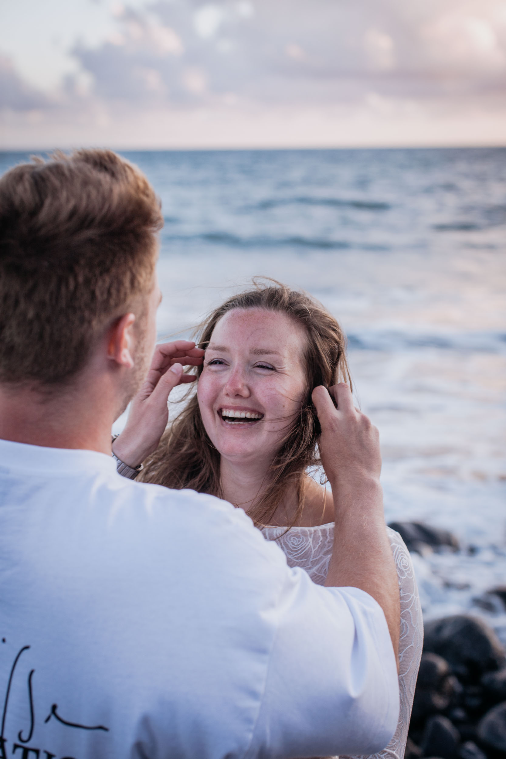 Vertical frame. He tucks a strand behind her ear and she laughs openly, the surf soft behind, Praia Formosa, Madeira