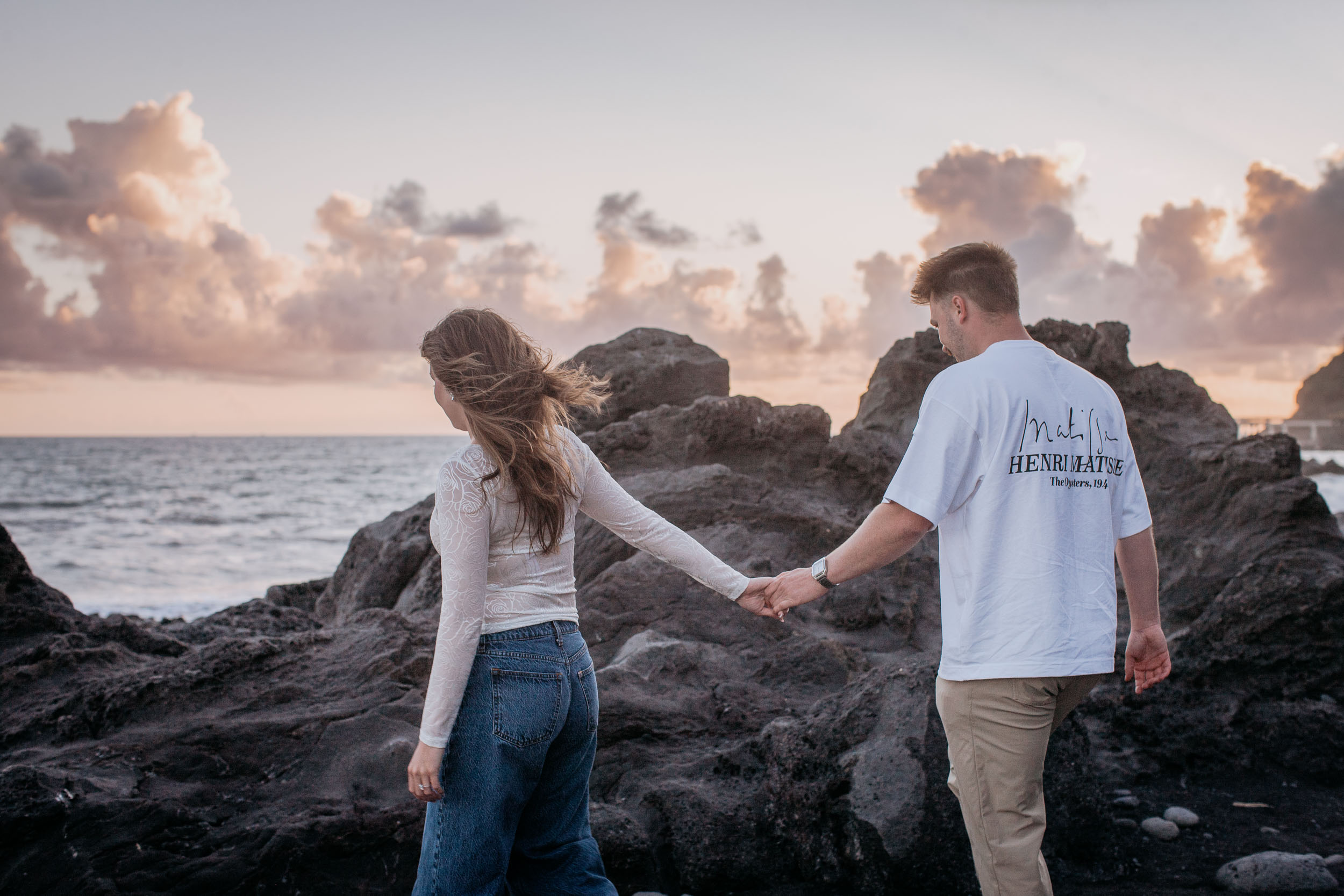 Rylie and Abby holding hands as they cross the dark volcanic rock formations at the west end of Praia Formosa, Funchal, Madeira