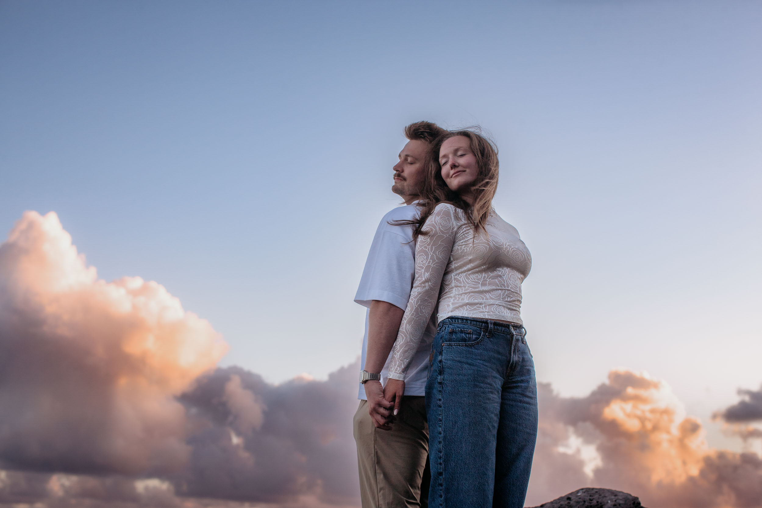 Rylie and Abby standing back to back with eyes closed, soft pink dusk clouds behind them, Praia Formosa, Madeira