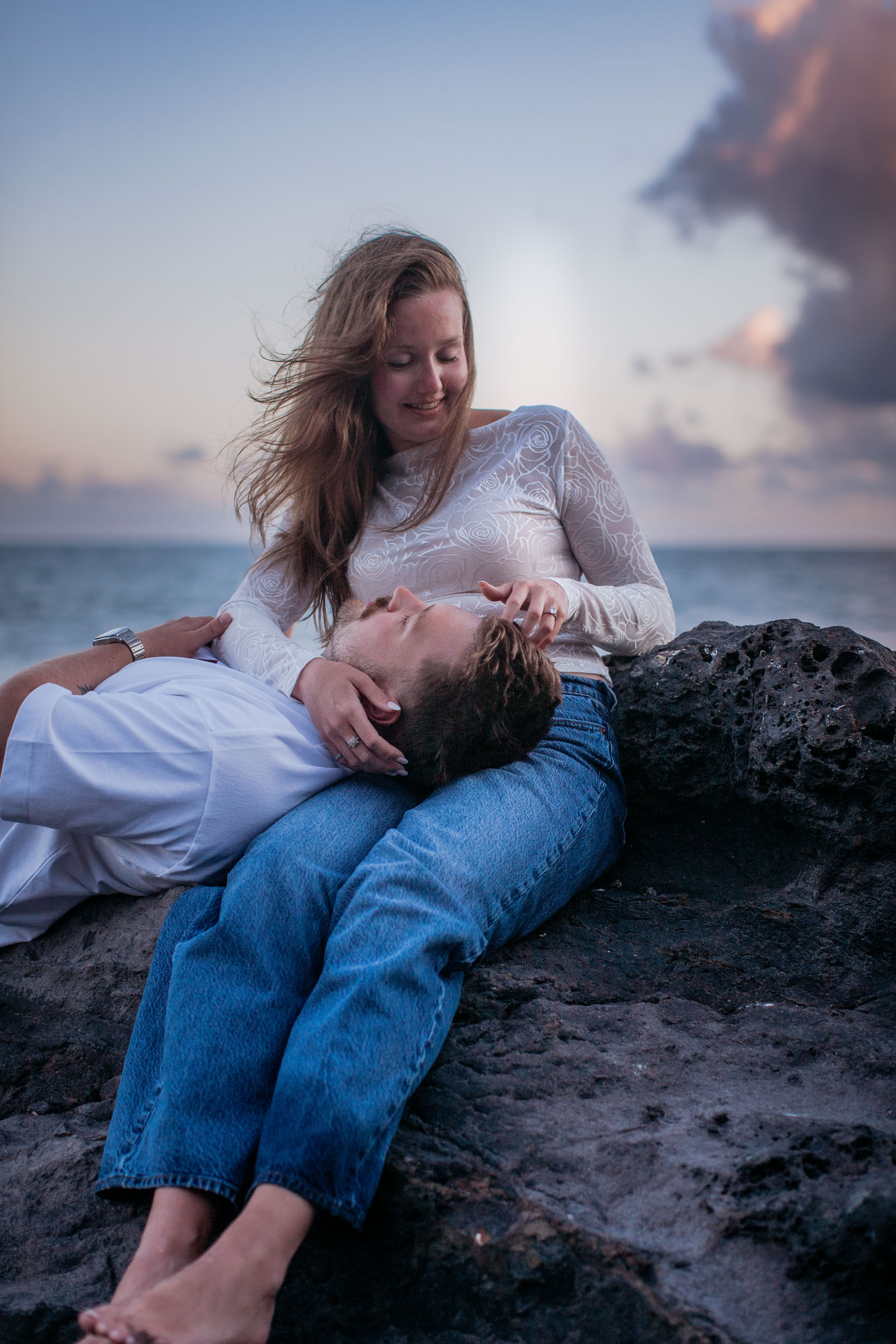Vertical frame. The same moment from the side, his eyes closed, her hair lit against the pale sky, Praia Formosa, Madeira