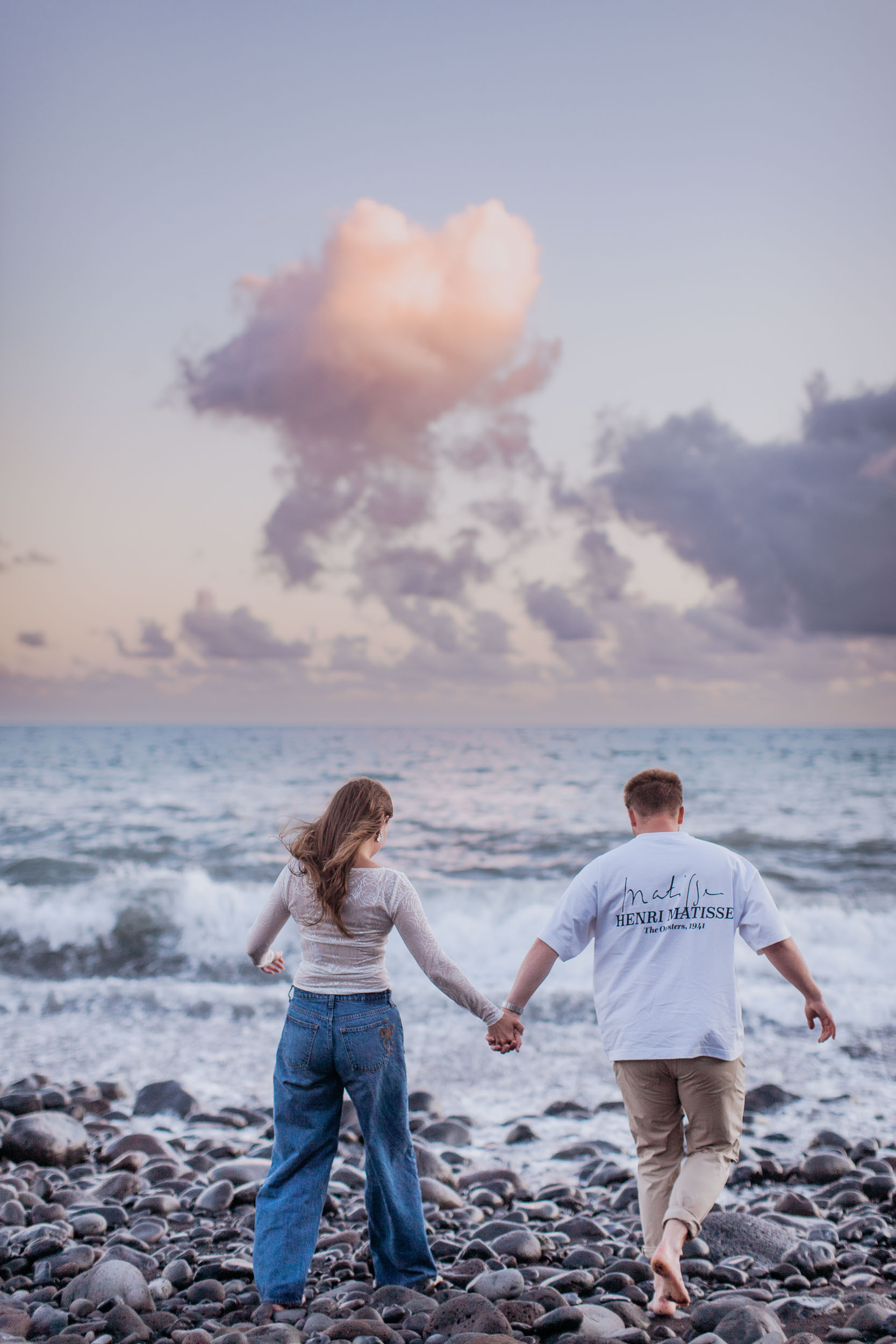 Rylie and Abby walking away from the camera into the Atlantic surf, soft pink and lavender dusk clouds above, Praia Formosa, Funchal, Madeira