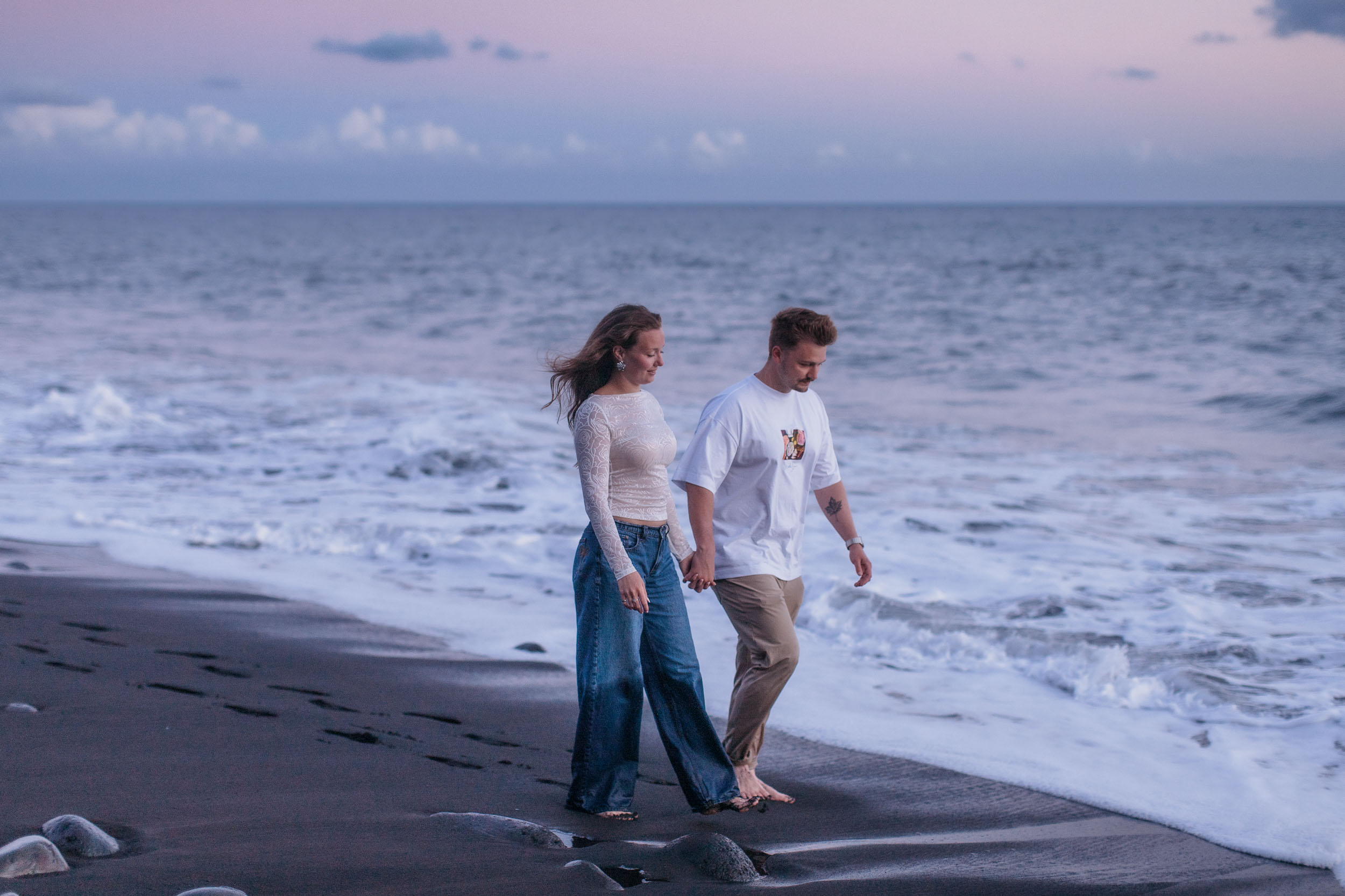Walking the waterline at dusk, the beach empty behind them and pink light on the clouds, Praia Formosa, Madeira