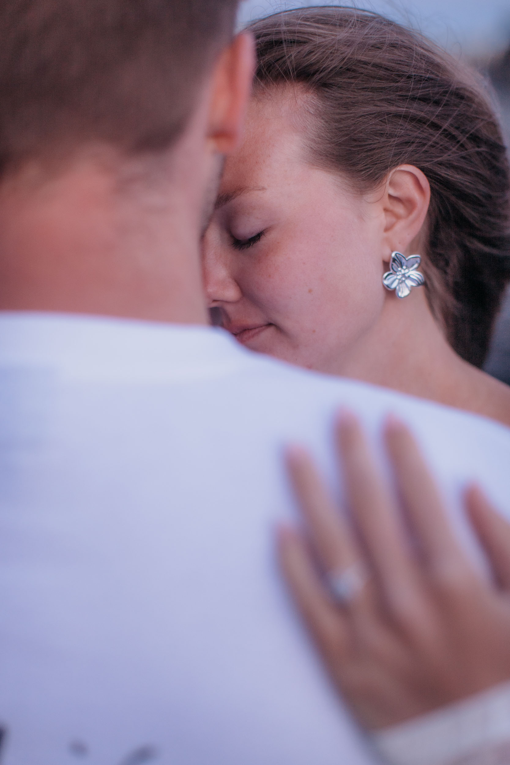 Vertical frame. Close over his shoulder, her eyes closed against his neck, her hand with the ring out of focus in front, Praia Formosa, Madeira