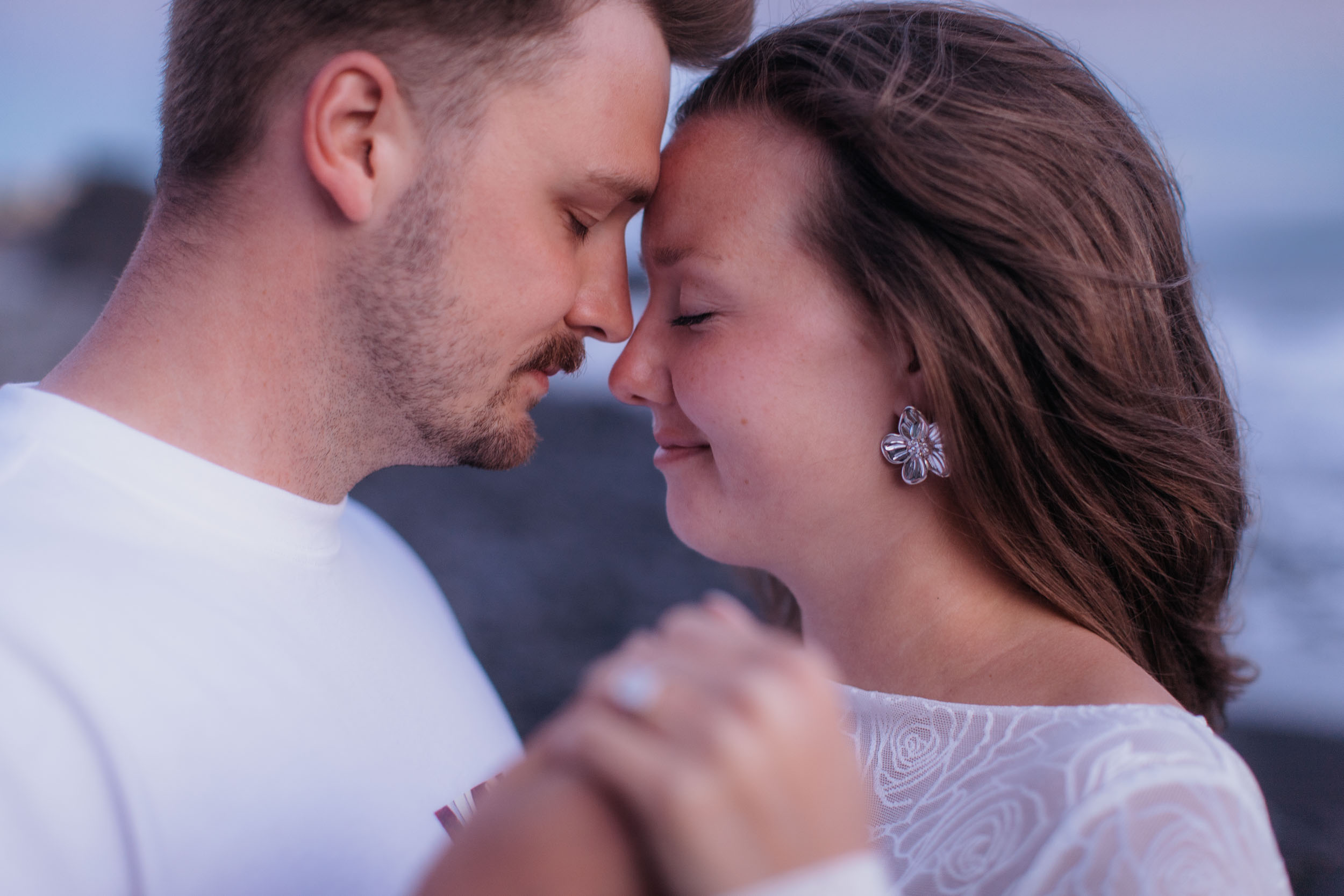 Close profile portrait, foreheads together, both with eyes closed, her hand held in his between them, Praia Formosa, Madeira