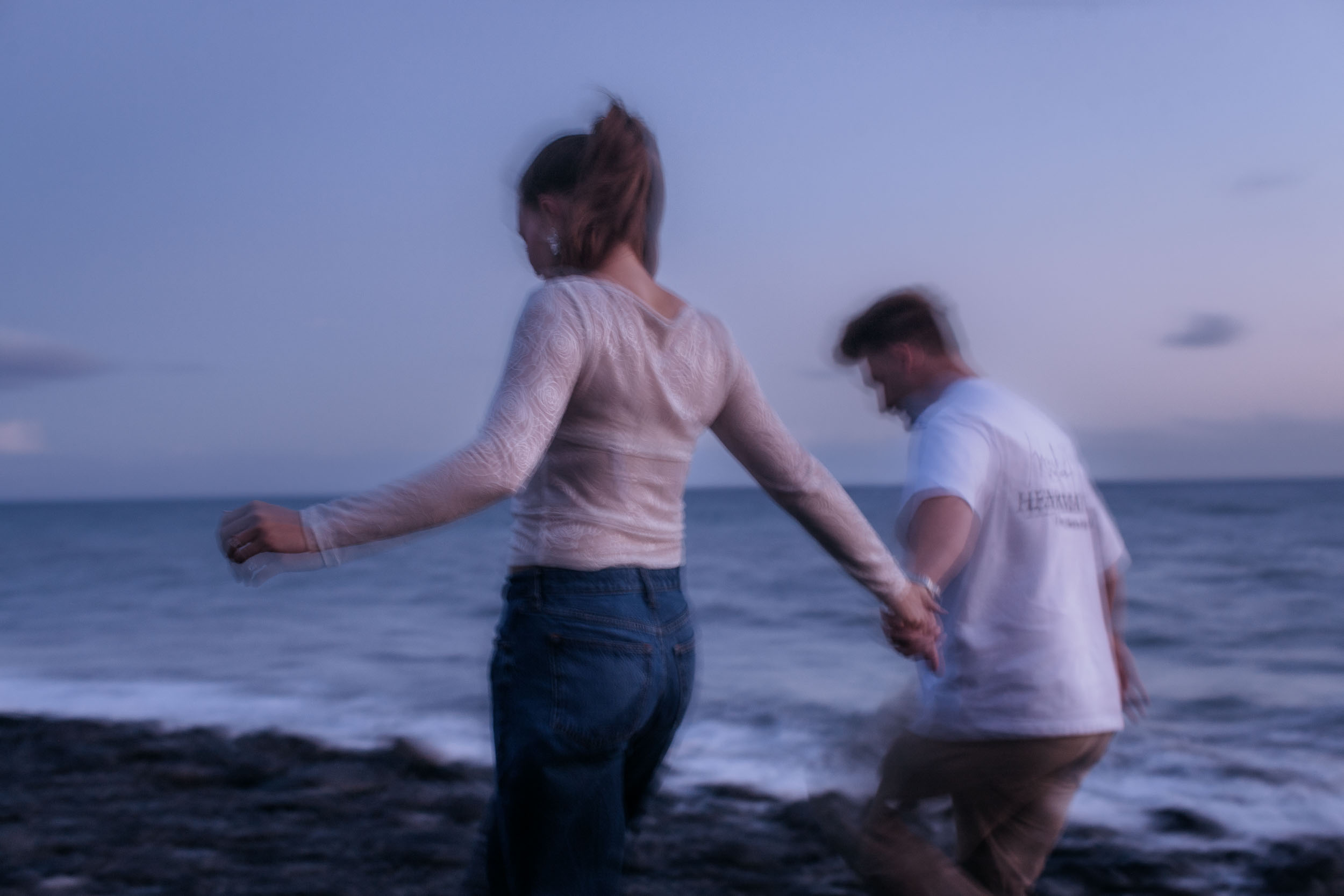 Deliberately blurred. The two of them turn away hand in hand along the waterline in the last light, Praia Formosa, Madeira