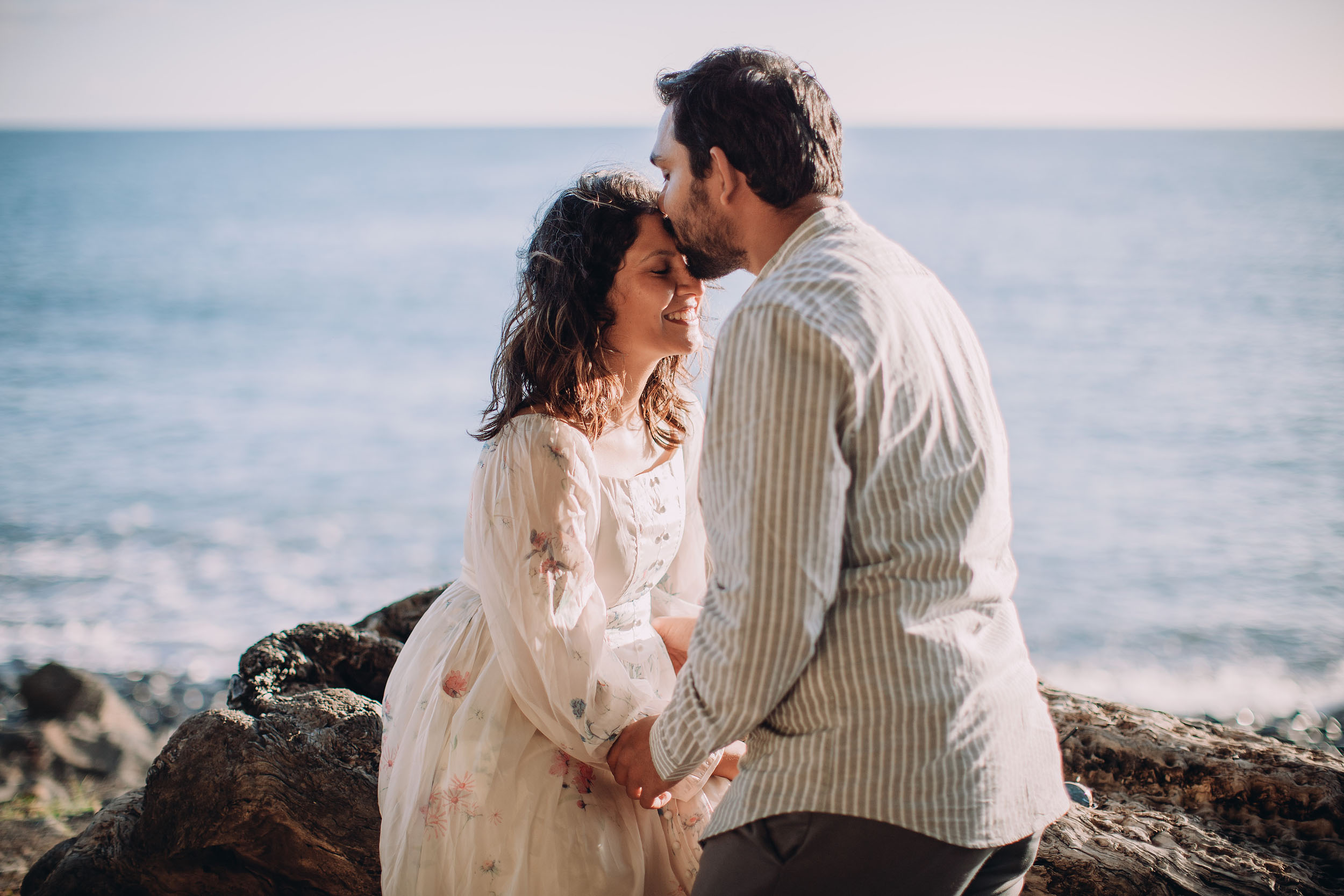 Saket kissing Sneha's forehead on volcanic rocks at Praia Formosa, Atlantic waves and golden light behind them, Madeira