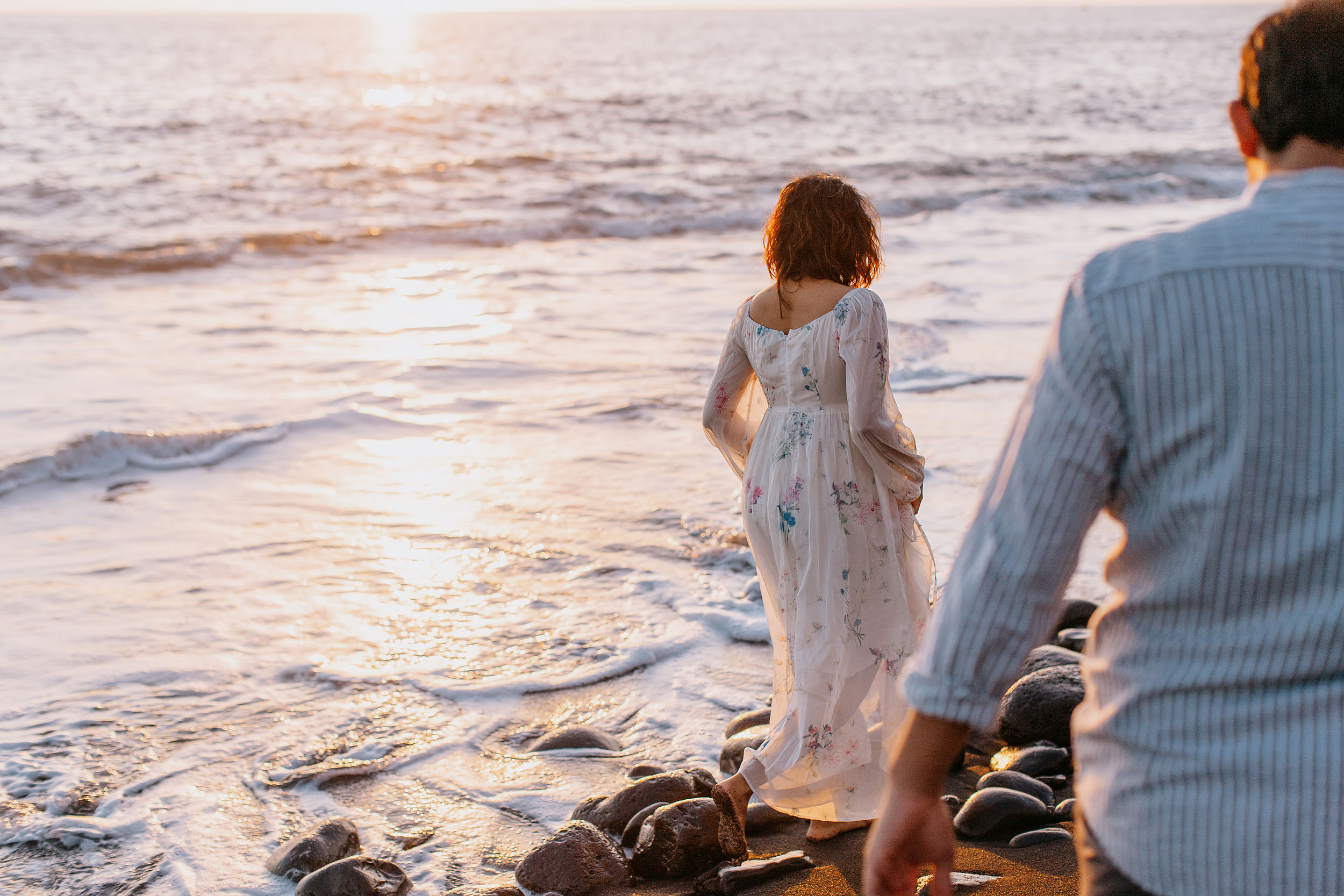 Sneha stepping into Atlantic waves at Praia Formosa, floral dress billowing in the sea breeze, golden sunset light on the water, Madeira