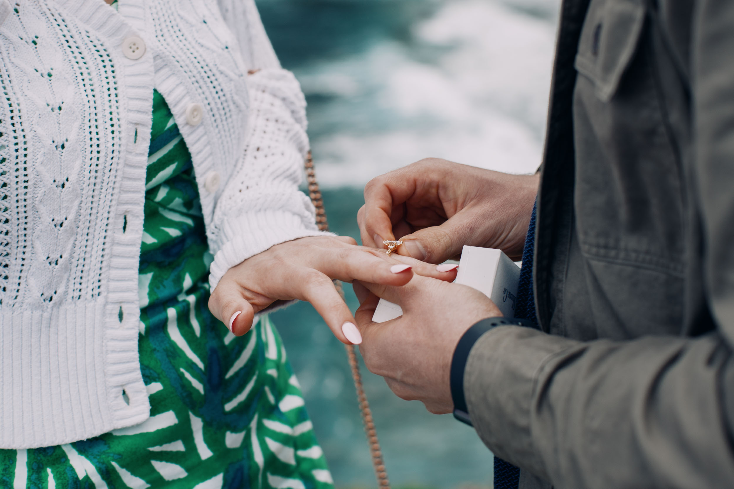 Man placing engagement ring on woman's hand at Miradouro do Guindaste cliff, Madeira