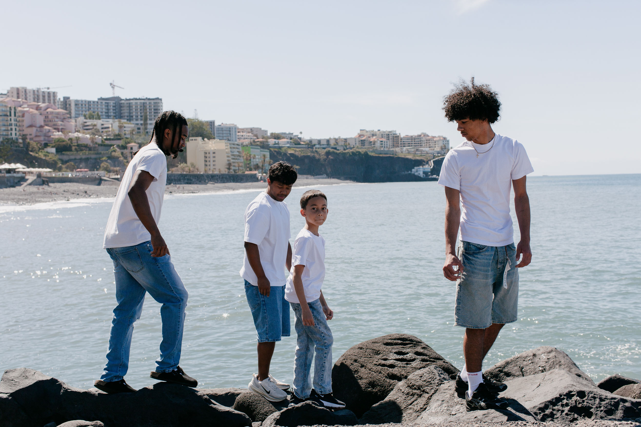 Four brothers on the volcanic rocks by the sea, the youngest looking to camera, Funchal coast behind, Praia Formosa, Madeira